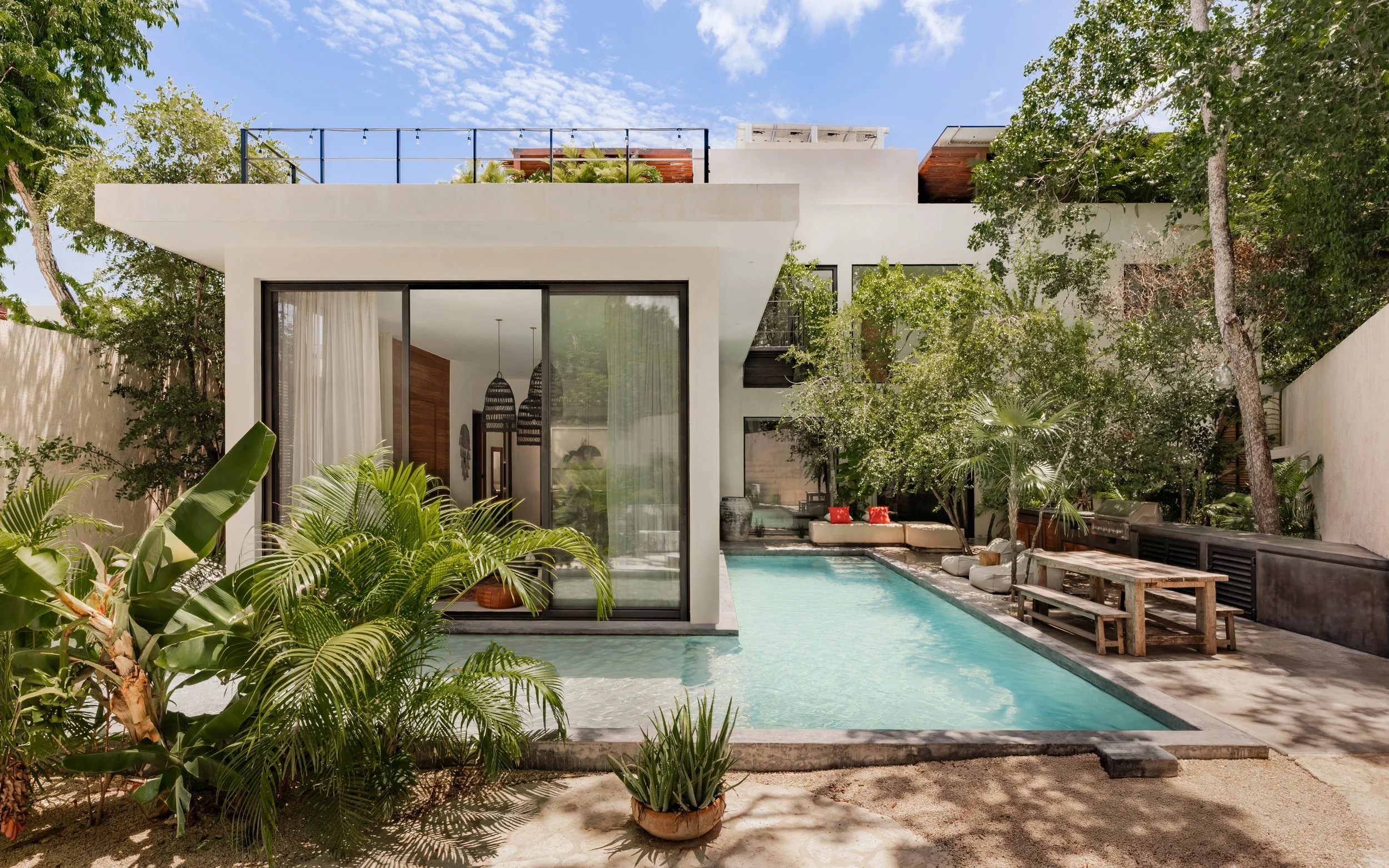 Modern house with a swimming pool, surrounded by greenery and trees, with sliding glass doors leading to the poolside interior.