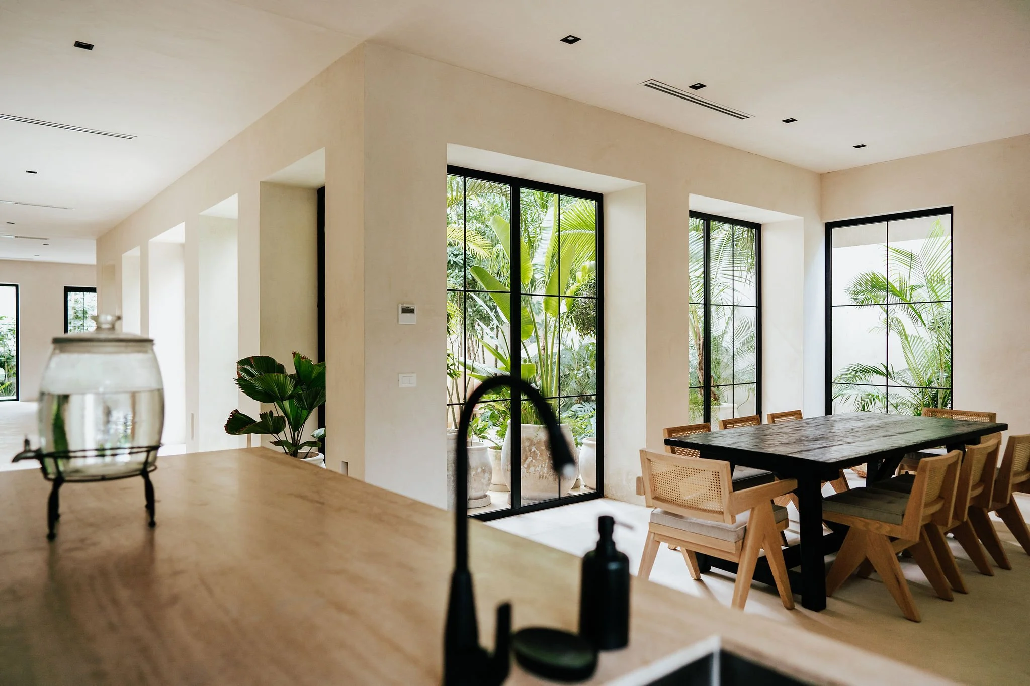 Modern interior dining area with large windows, green plants, and wooden furniture.