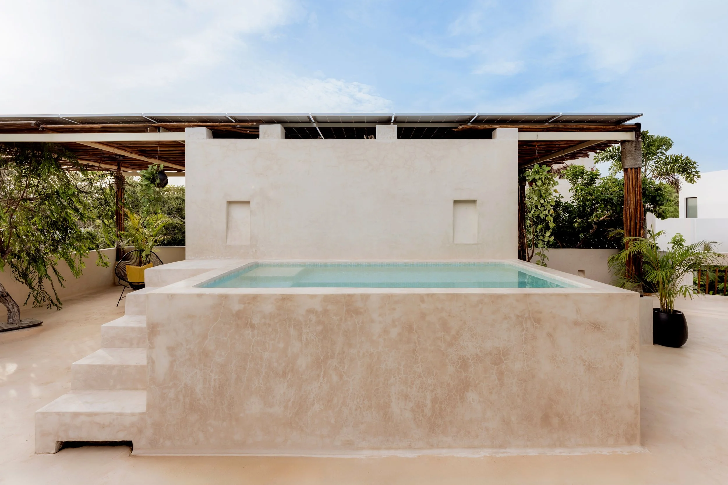 Modern house with a swimming pool and green plants, under a blue sky.