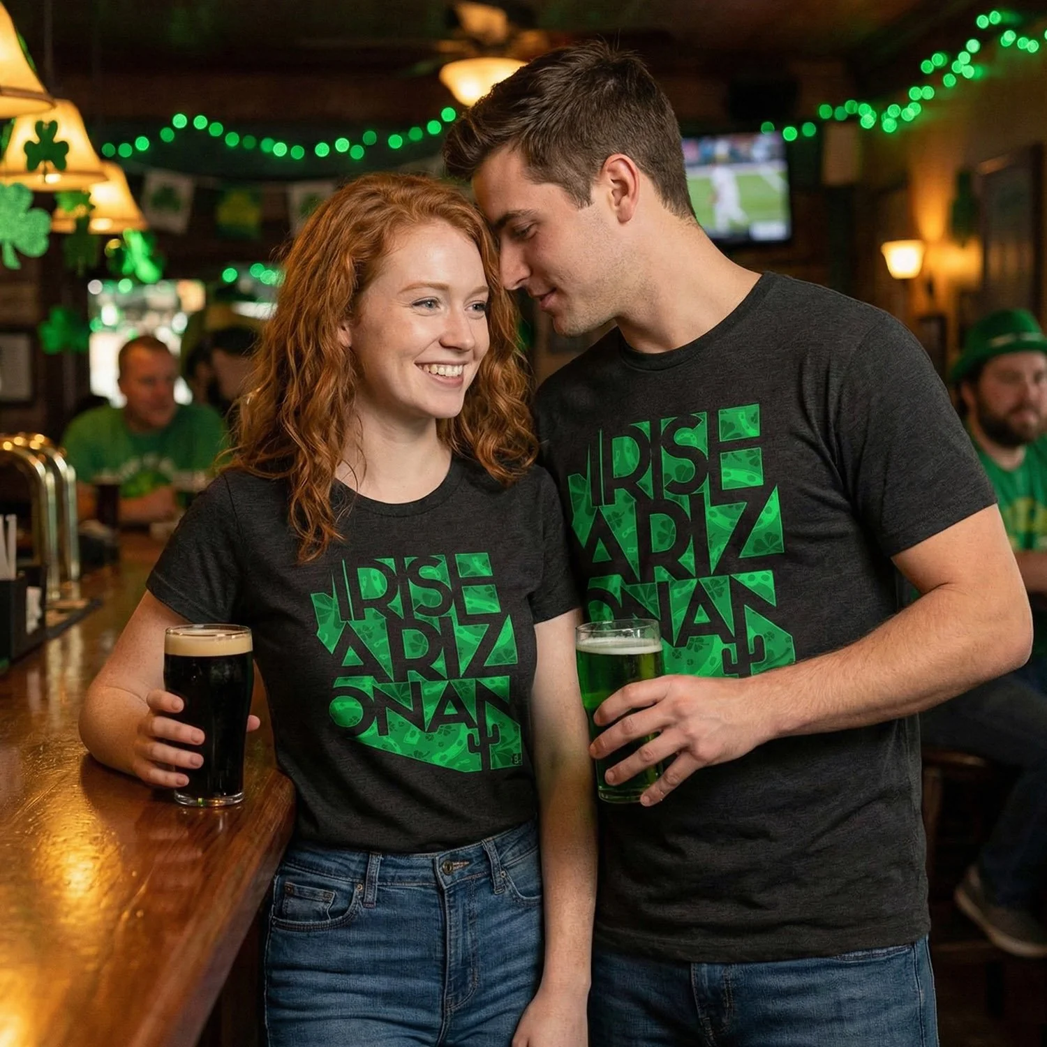 A young woman and man in a bar celebrating St. Patrick's Day, wearing matching black T-shirts with green shamrocks and the words 'Rise Arkansas.' They are smiling, holding pints of dark and green beer, with green decorations and other patrons visible in the background.