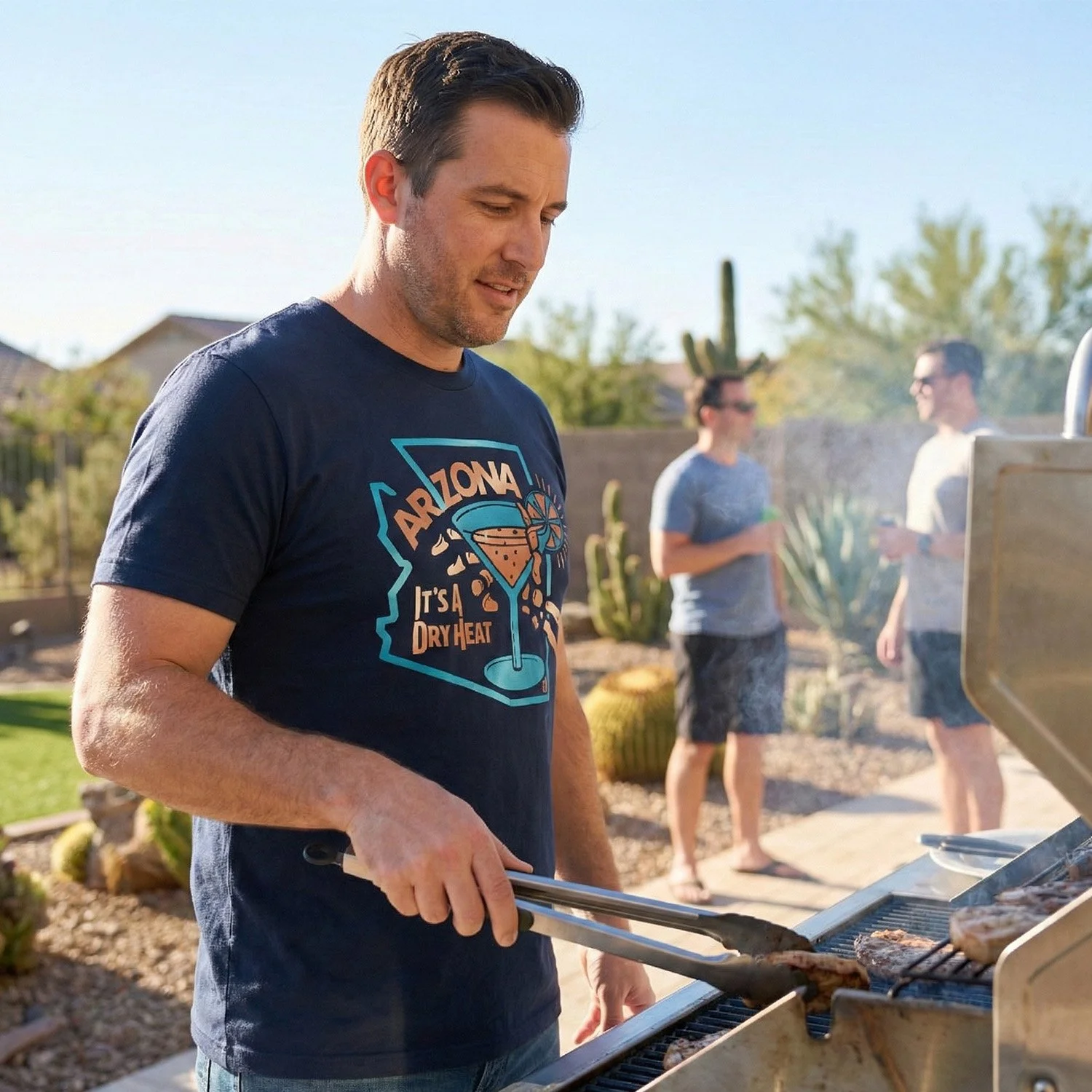 A man grilling meat on a barbecue outdoors during the daytime, with two people in the background chatting near desert plants.