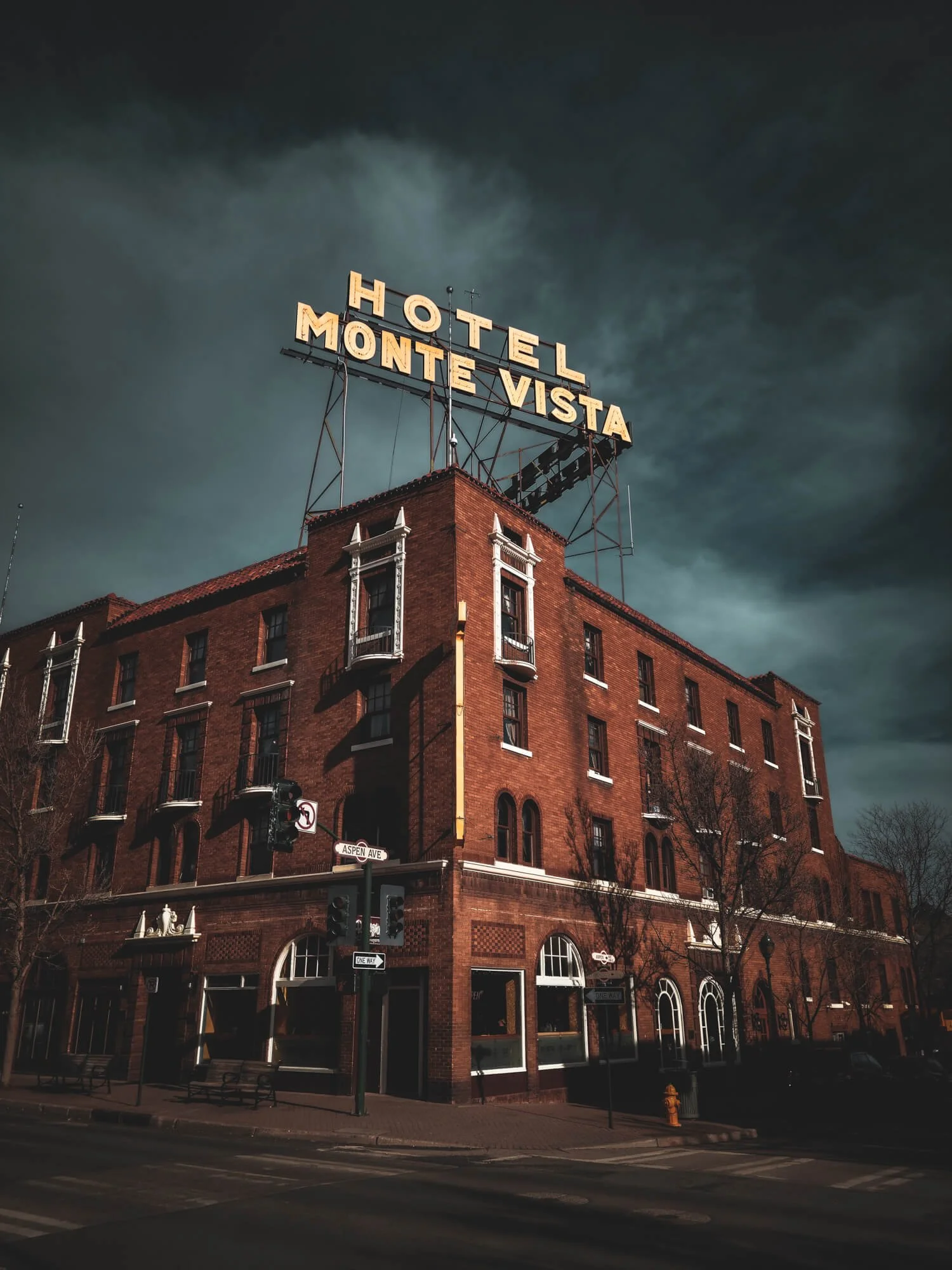 Brick building with a yellow sign on top that reads 'HOTEL MONTE VISTA' against a dark sky.