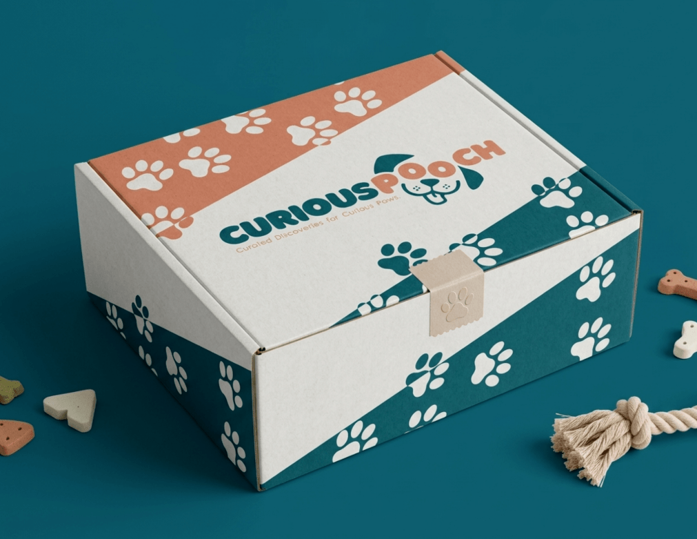 A box labeled 'Curious Pooch' with paw print and dog face logo, surrounded by dog treats and a rope toy, on a blue surface.