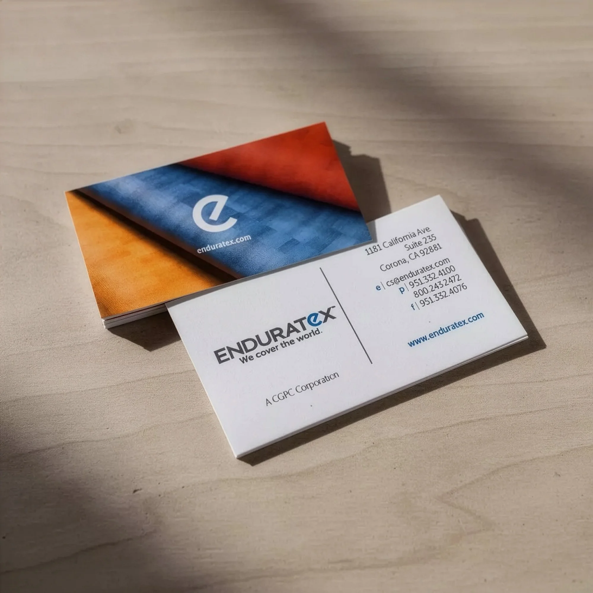 Business cards for Enduratex on a wooden surface, featuring contact information and logo.