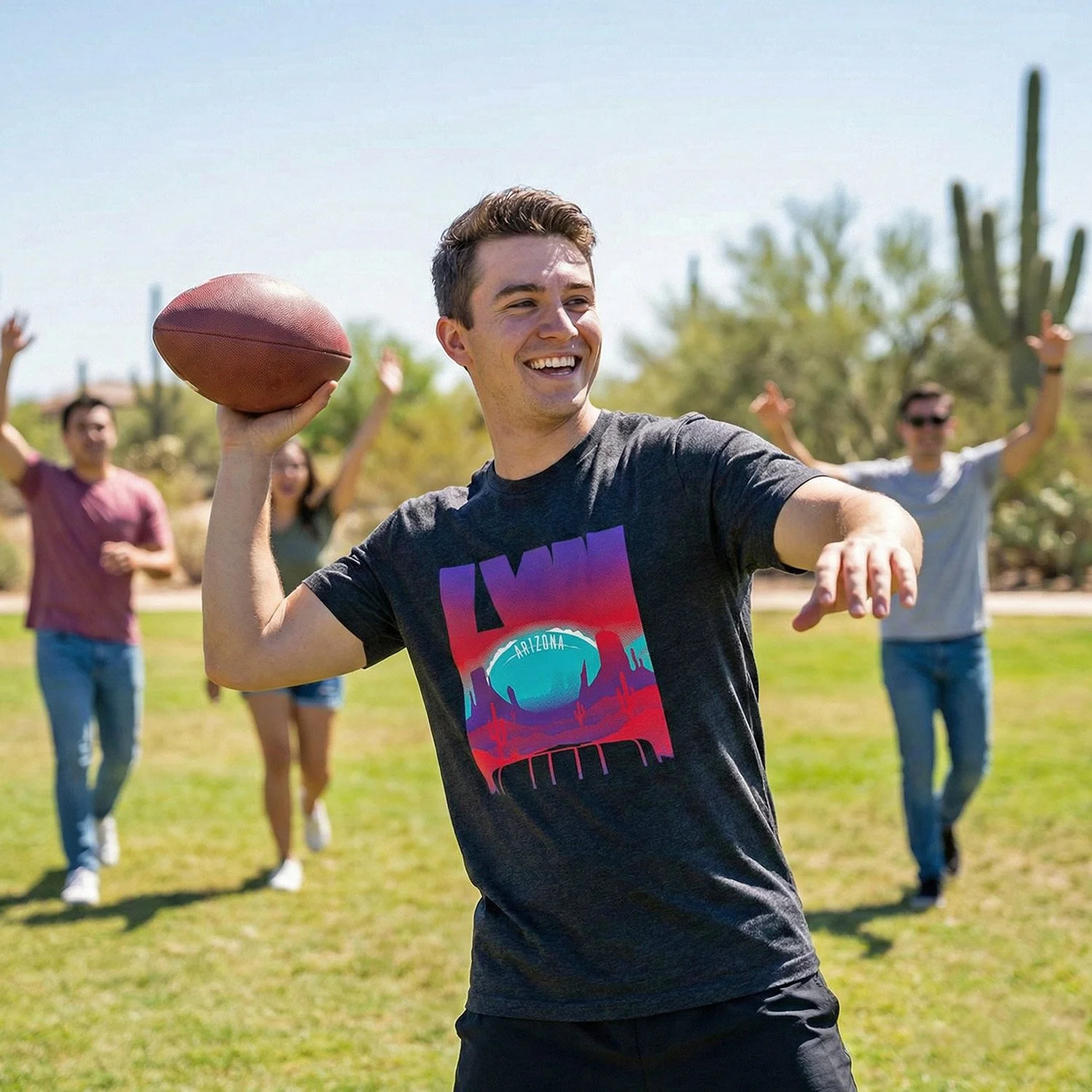Young man in a dark gray T-shirt holding an American football, smiling, with a group of friends in the background in a desert landscape with cacti.