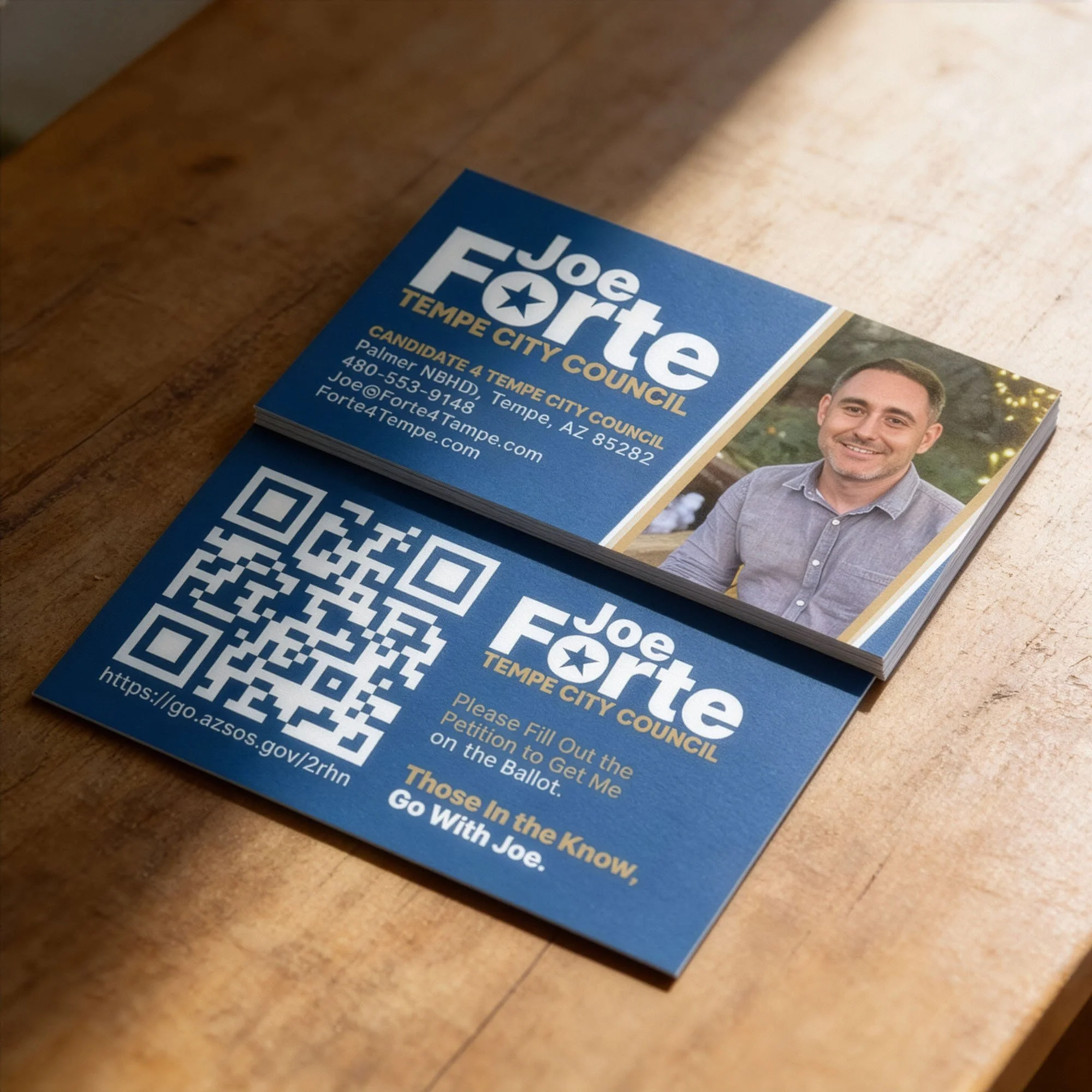 Political campaign flyers for Joe Forte, a candidate for Tempe City Council, showing his name, position, contact information, a photo of him smiling, and a QR code with a URL to a voting webpage. The flyers are on a wooden surface.