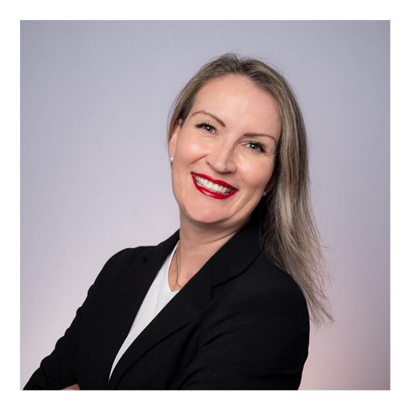 Bettina L. Lippisc, AIGP, CIPM - A woman with shoulder-length wavy blonde hair, wearing a black blazer and white top, smiling with red lipstick against a plain light gray background.