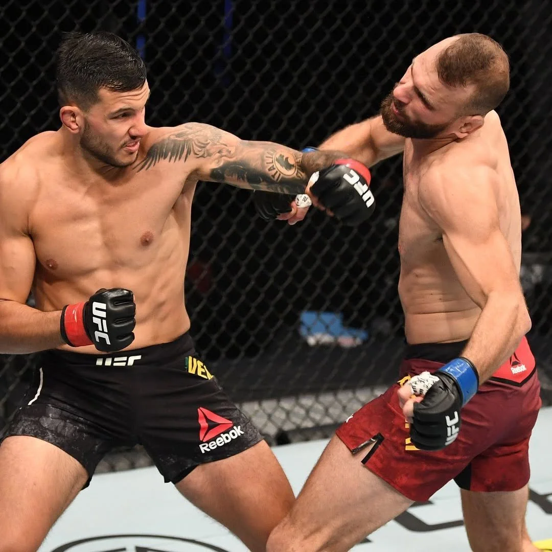 Two mixed martial arts fighters in an intense exchange inside the octagon, with one fighter landing a punch on the other.
