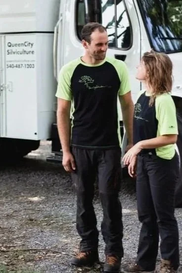 A man and a young girl are standing outdoors, smiling at each other near a truck with the sign 'Queen City Silviculture.'