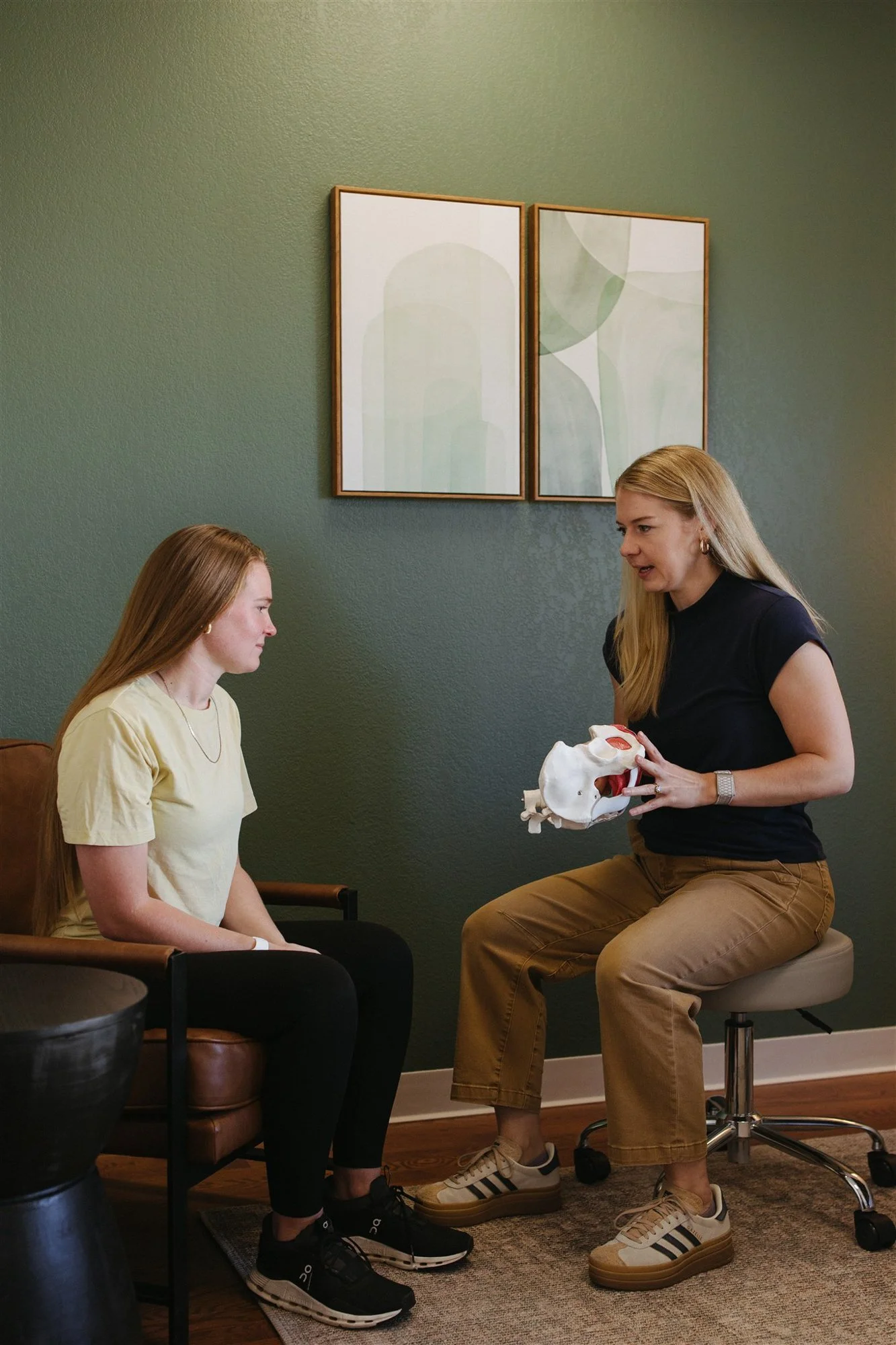 Mallory Willis a pelvic floor therapist talking to a patient and holding a pelvis anatomy model