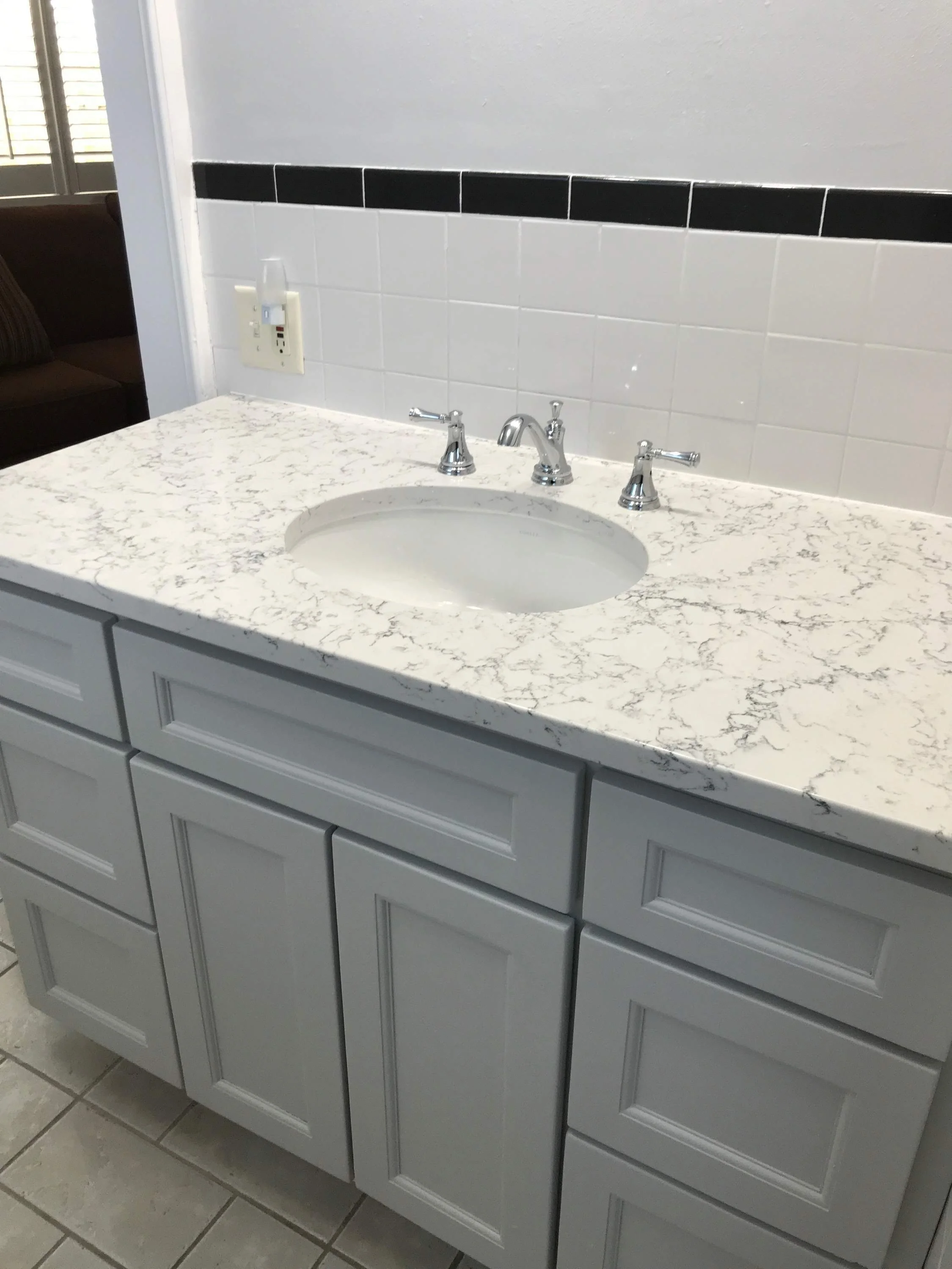 custom built Bathroom vanity with a marble countertop, an oval sink, and silver faucet, with light gray cabinets below.