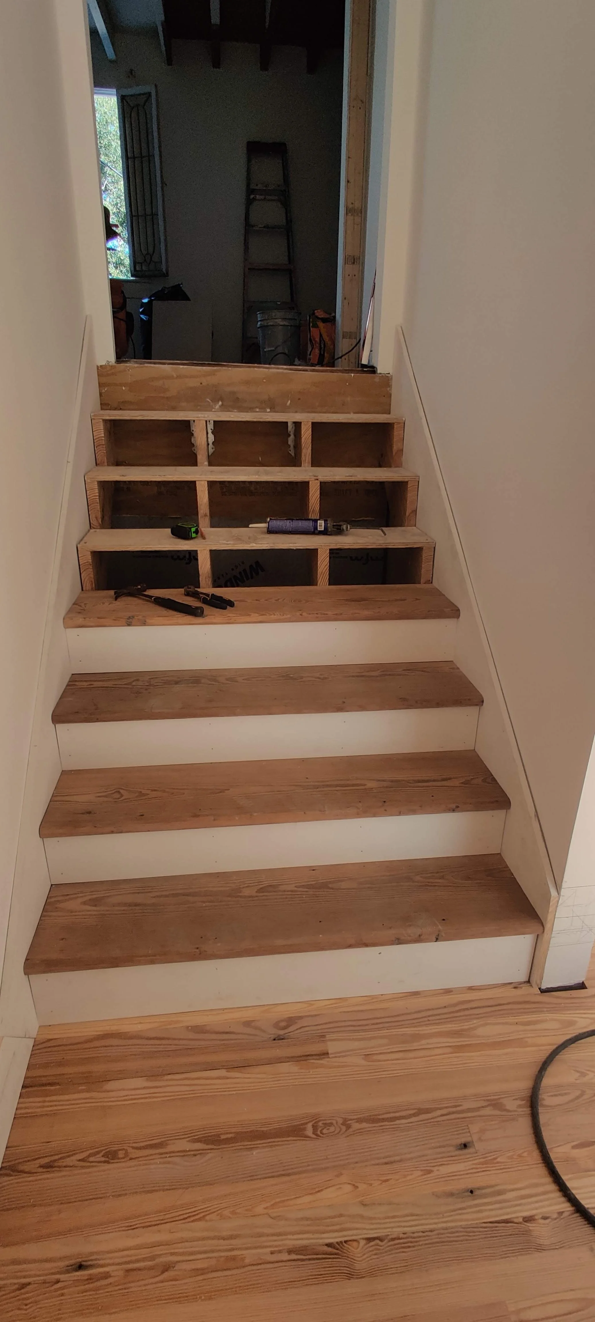 Wooden staircase in progress with steps partially installed, construction tools and supplies visible.