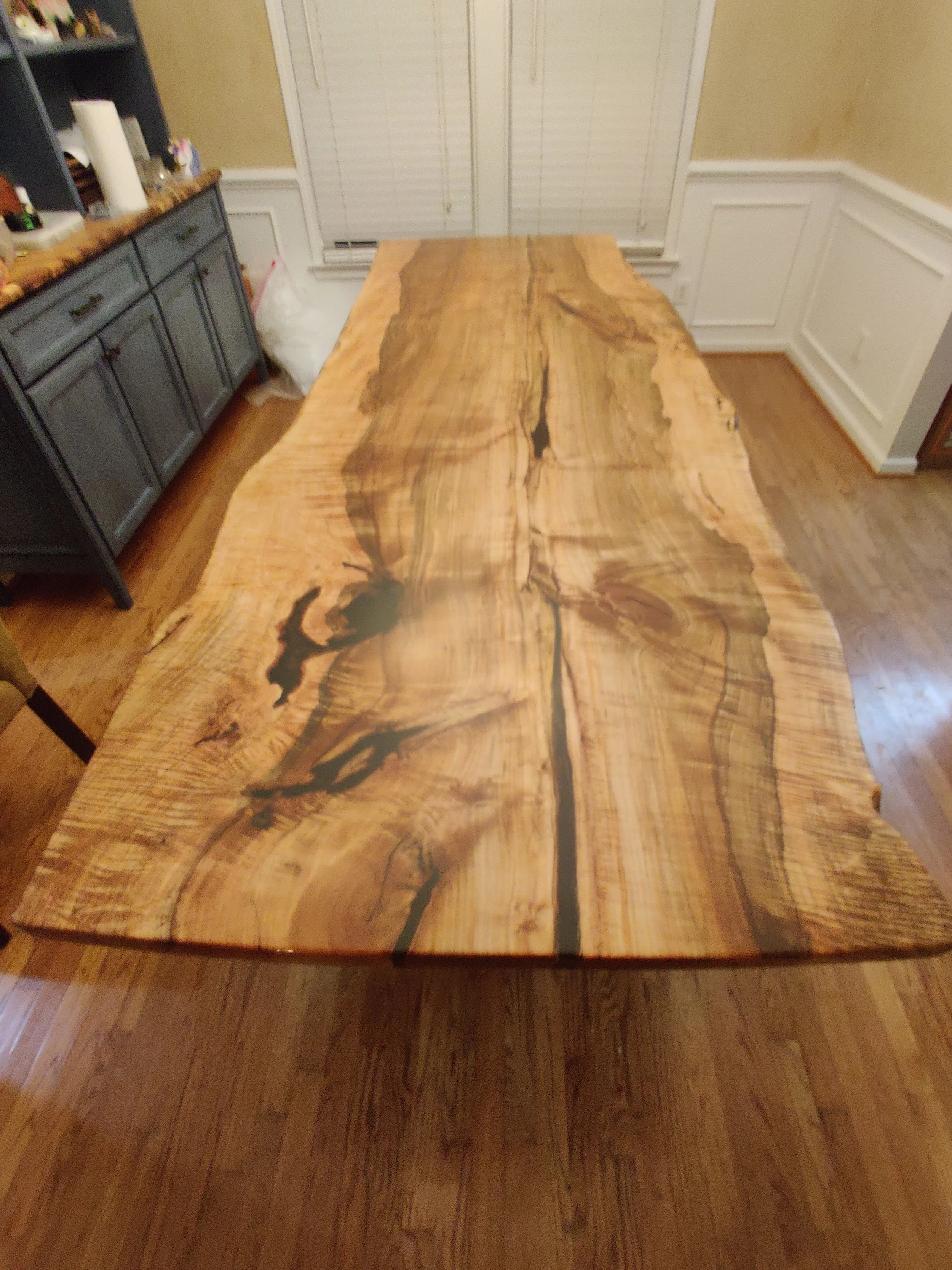A large wooden dining table with a natural, live edge design in a room with hardwood floors, white trim, and a blue cabinet.