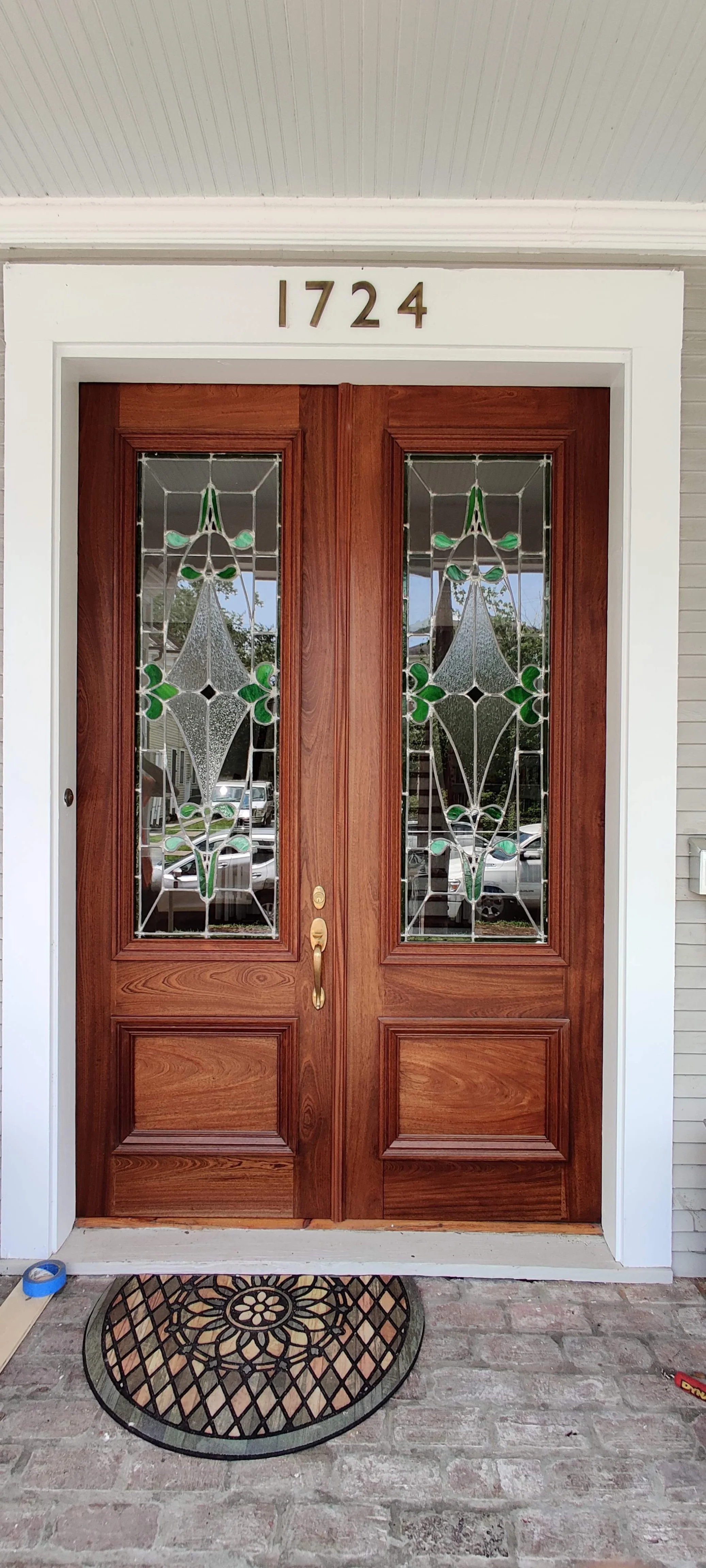 Front door with stained glass windows and house number 1724 above it, with a weathered doormat and brick porch.