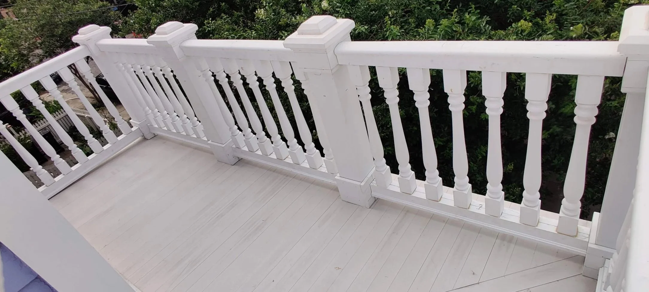 White wooden balcony railing with turned spindles and post caps, overlooking a lush green garden.