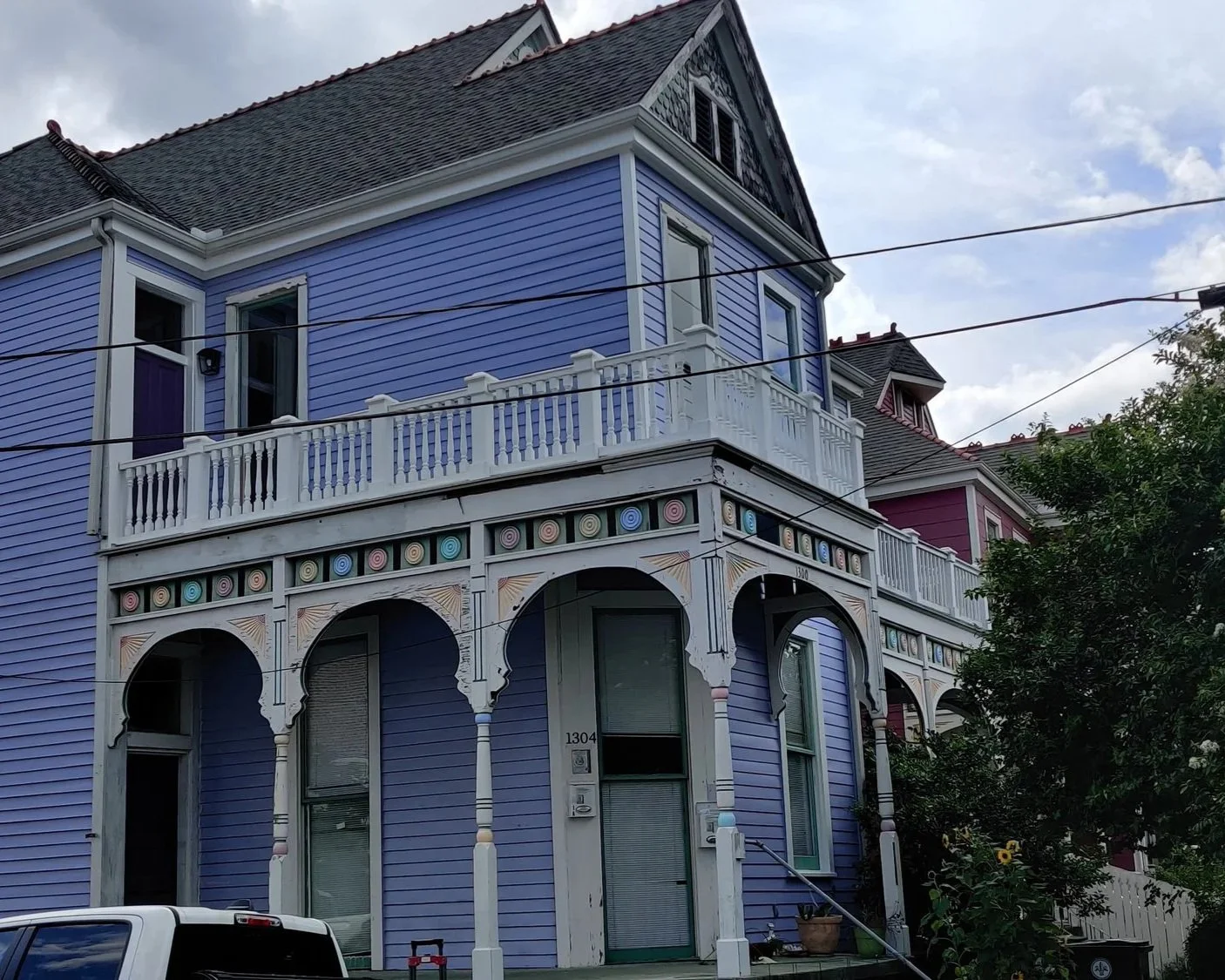 A colorful two-story house painted in shades of blue and purple with decorative trim and a balcony on the upper level.