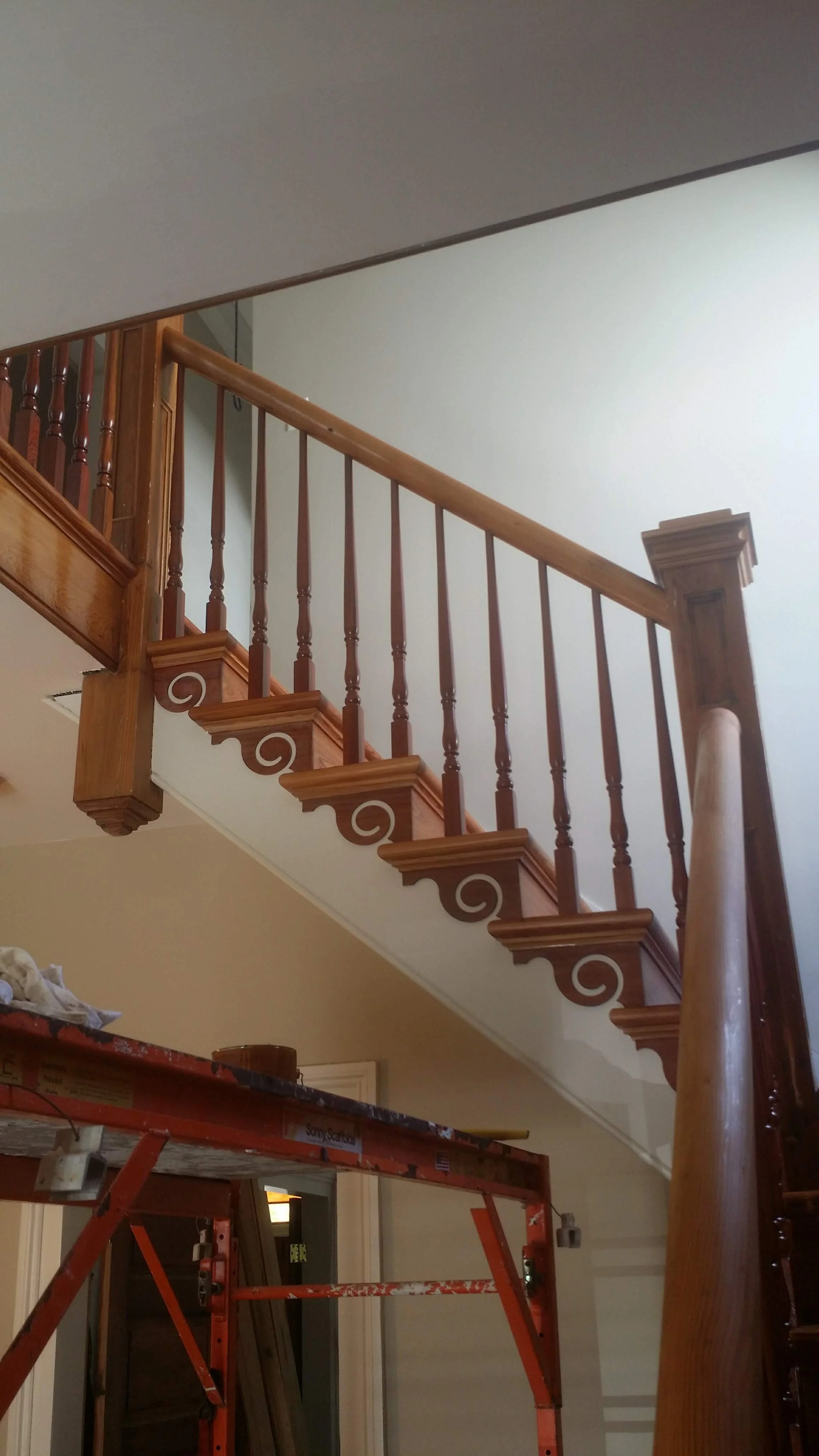Wooden staircase railing with decorative spindles and a scaffold in the foreground.