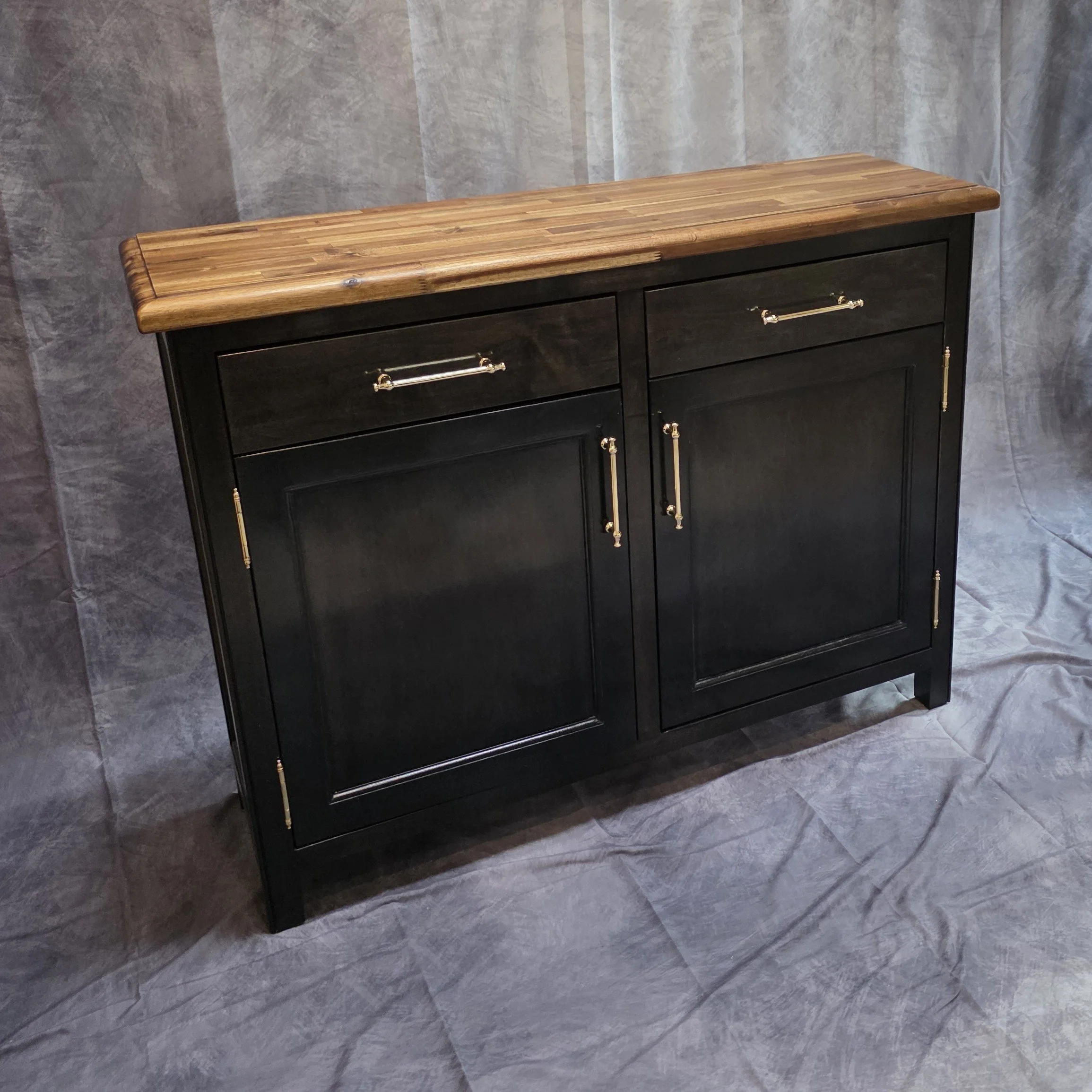 Black and brown wooden cabinet with metal handles and hinges, placed on a wrinkled gray fabric backdrop.