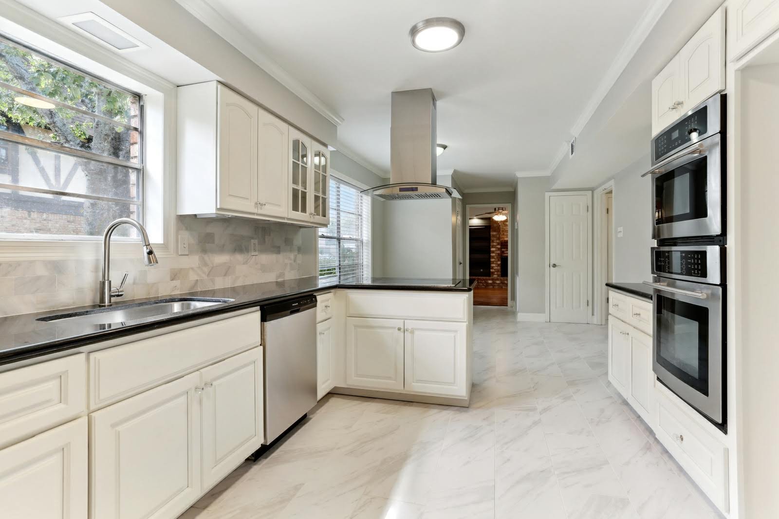 custom kitchen with white cabinets, stainless steel appliances, marble floor, and windows let in natural light.
