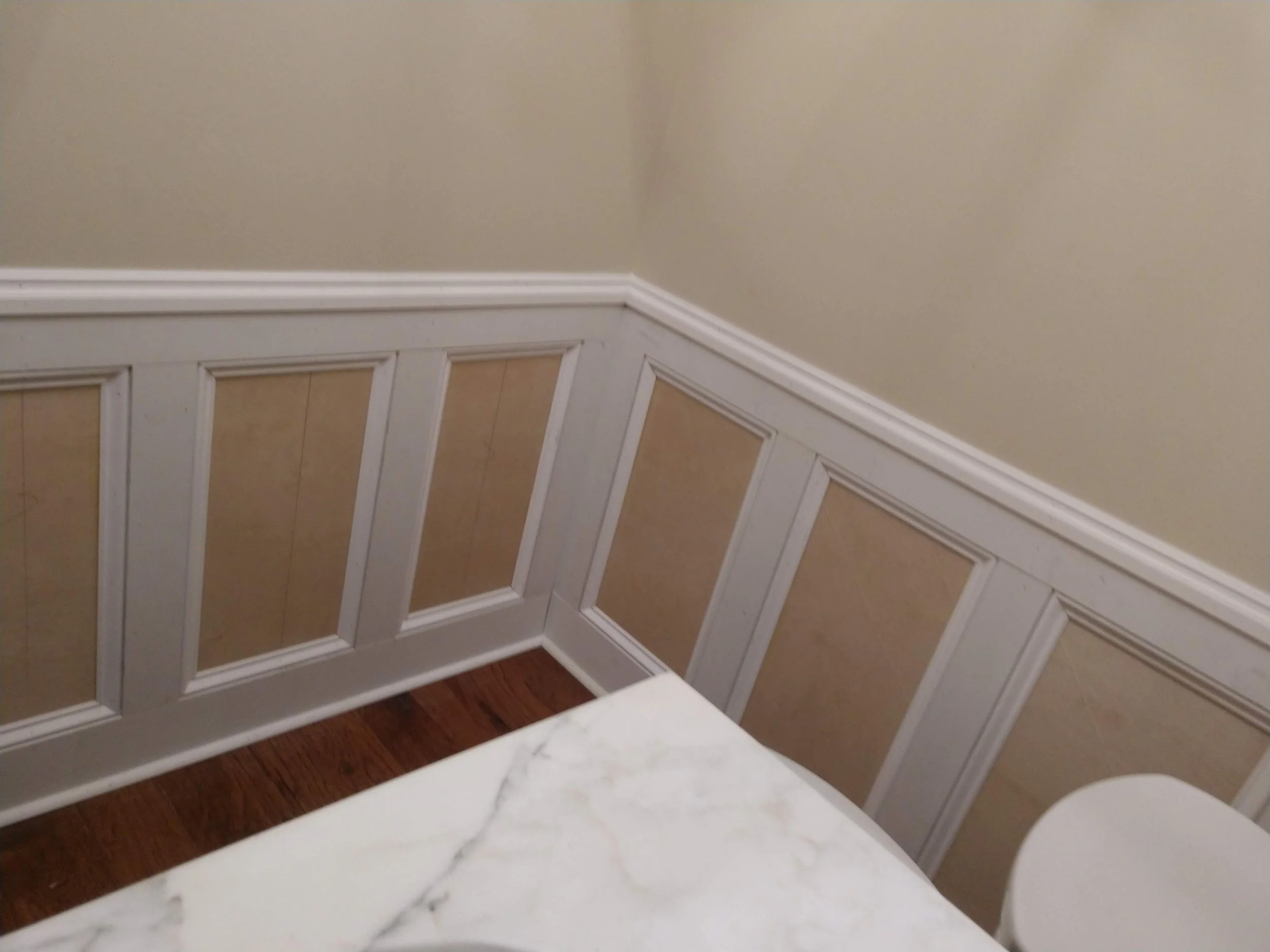 A small bathroom with beige walls, custom white wainscoting, 