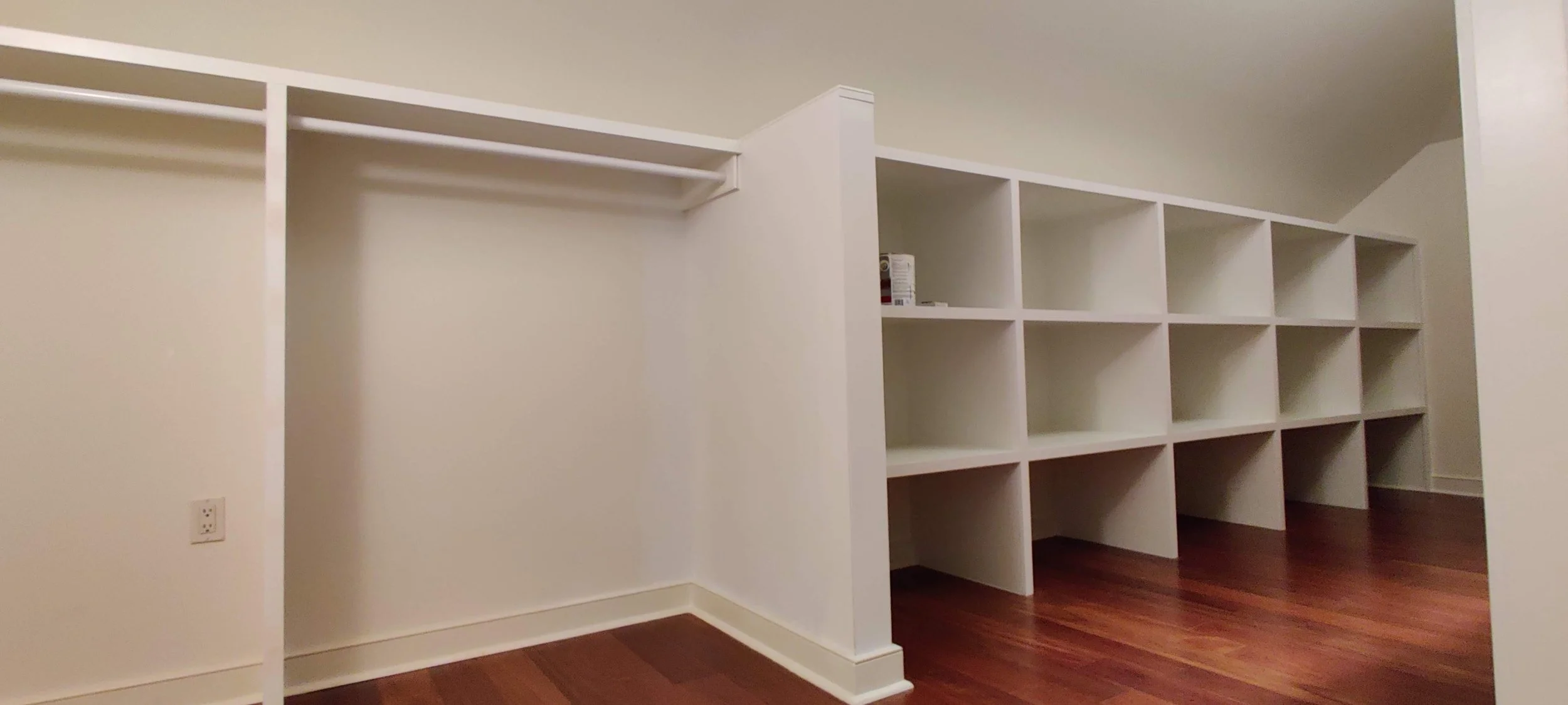 Empty walk-in closet with white shelving units and dark hardwood floors.