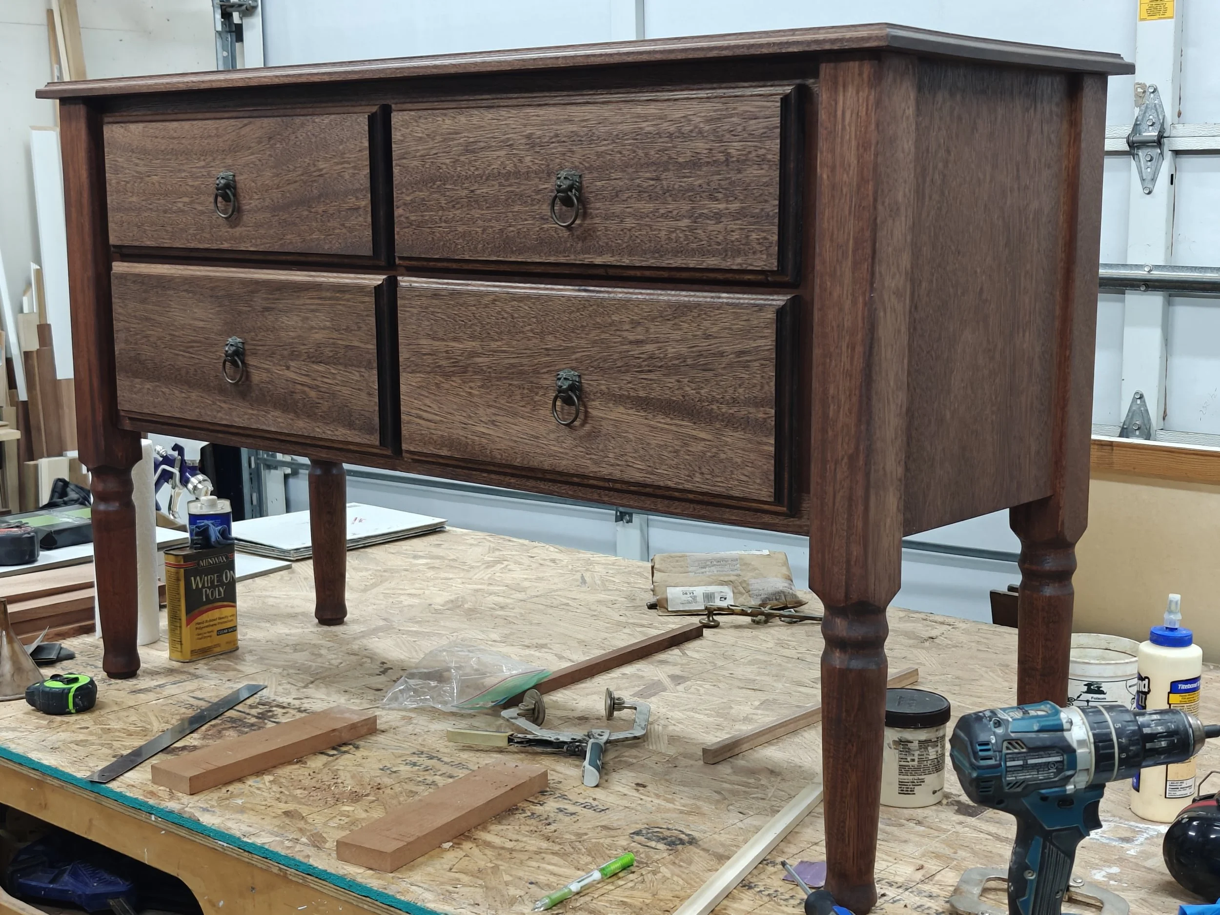 A mahogany side table with four drawers, in a workshop setting, with tools and supplies around it.