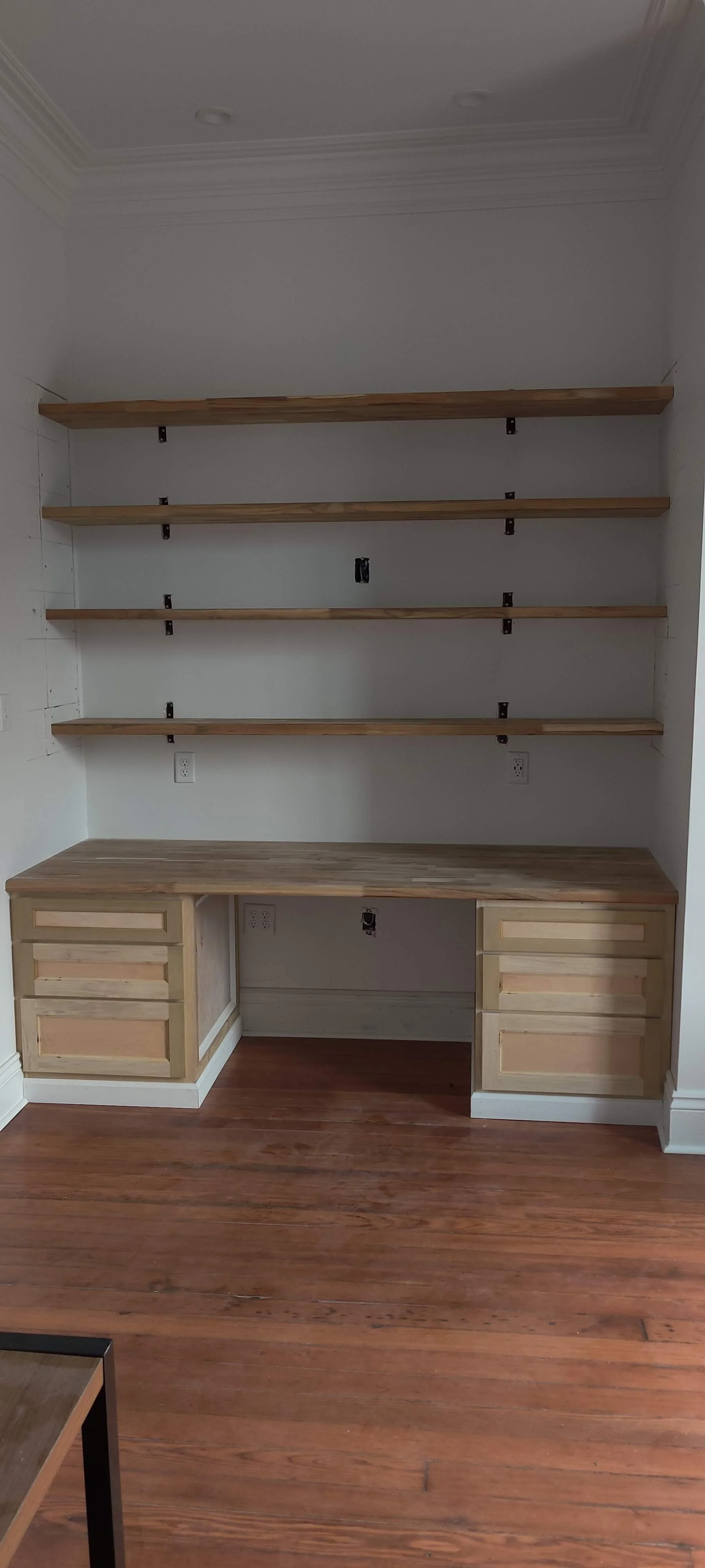 Empty built-in desk with wooden shelves on white walls and wooden floor.