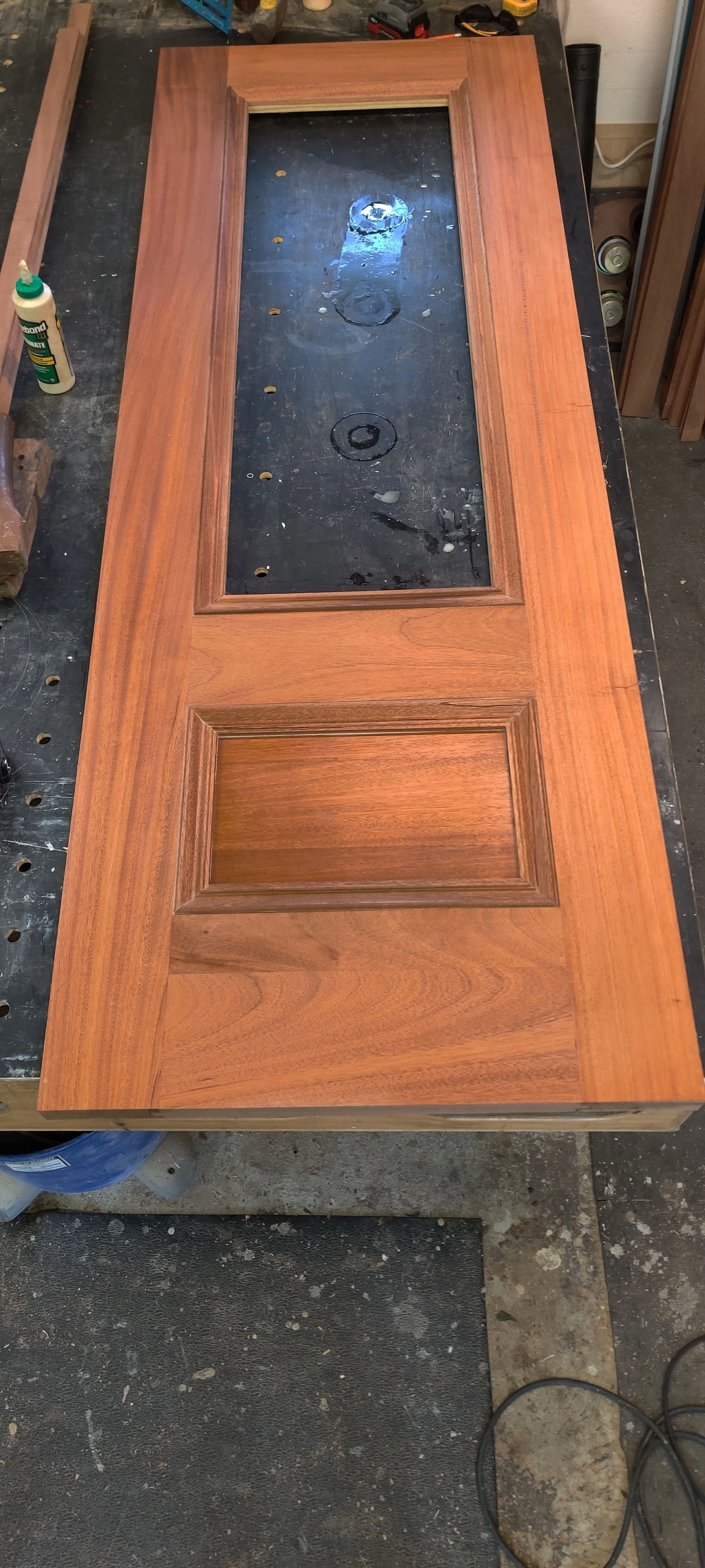 A wooden door with glass inset laying flat on a workbench in a workshop.