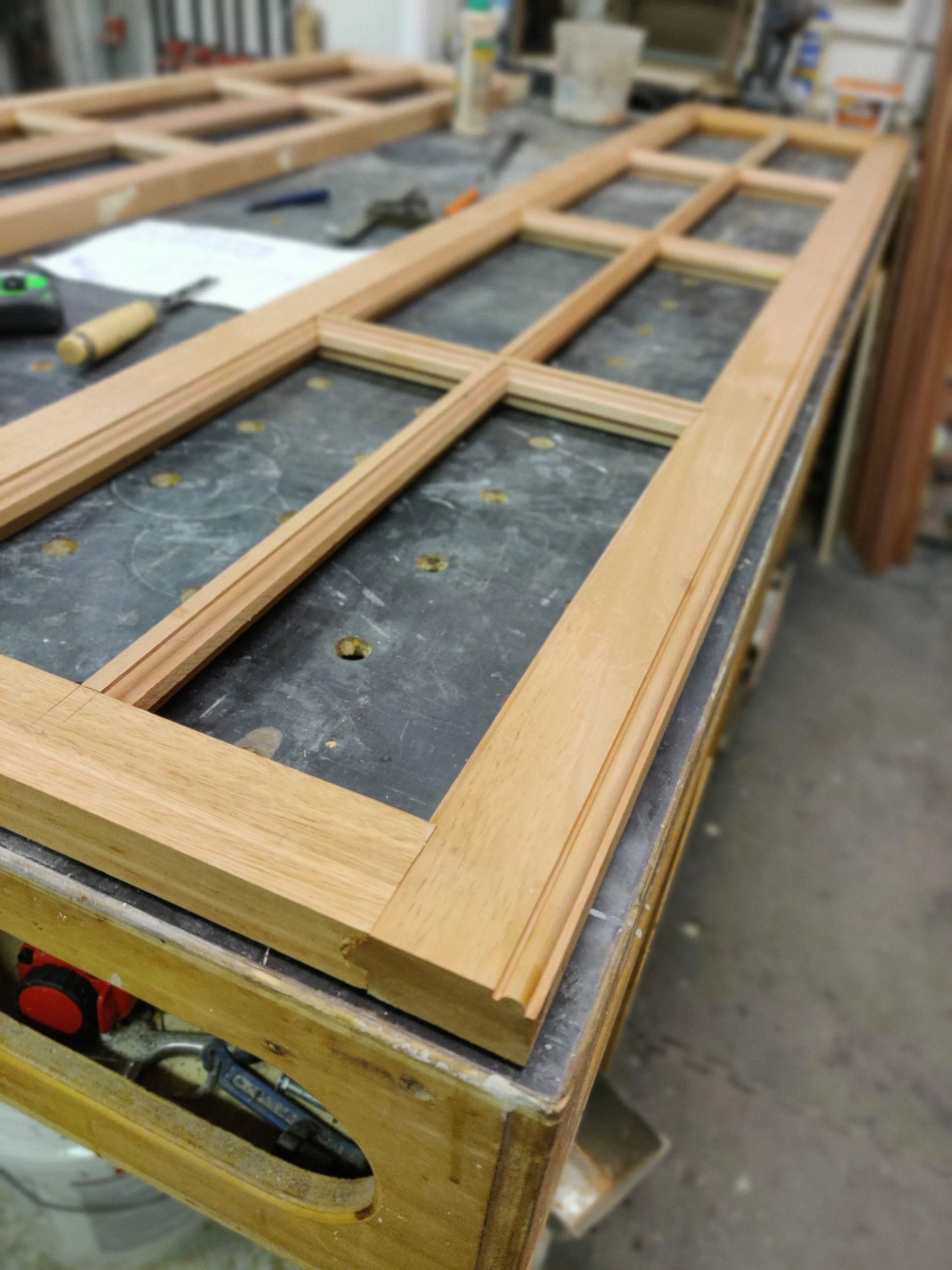 Wooden window frame being assembled on a workbench in a woodworking shop.
