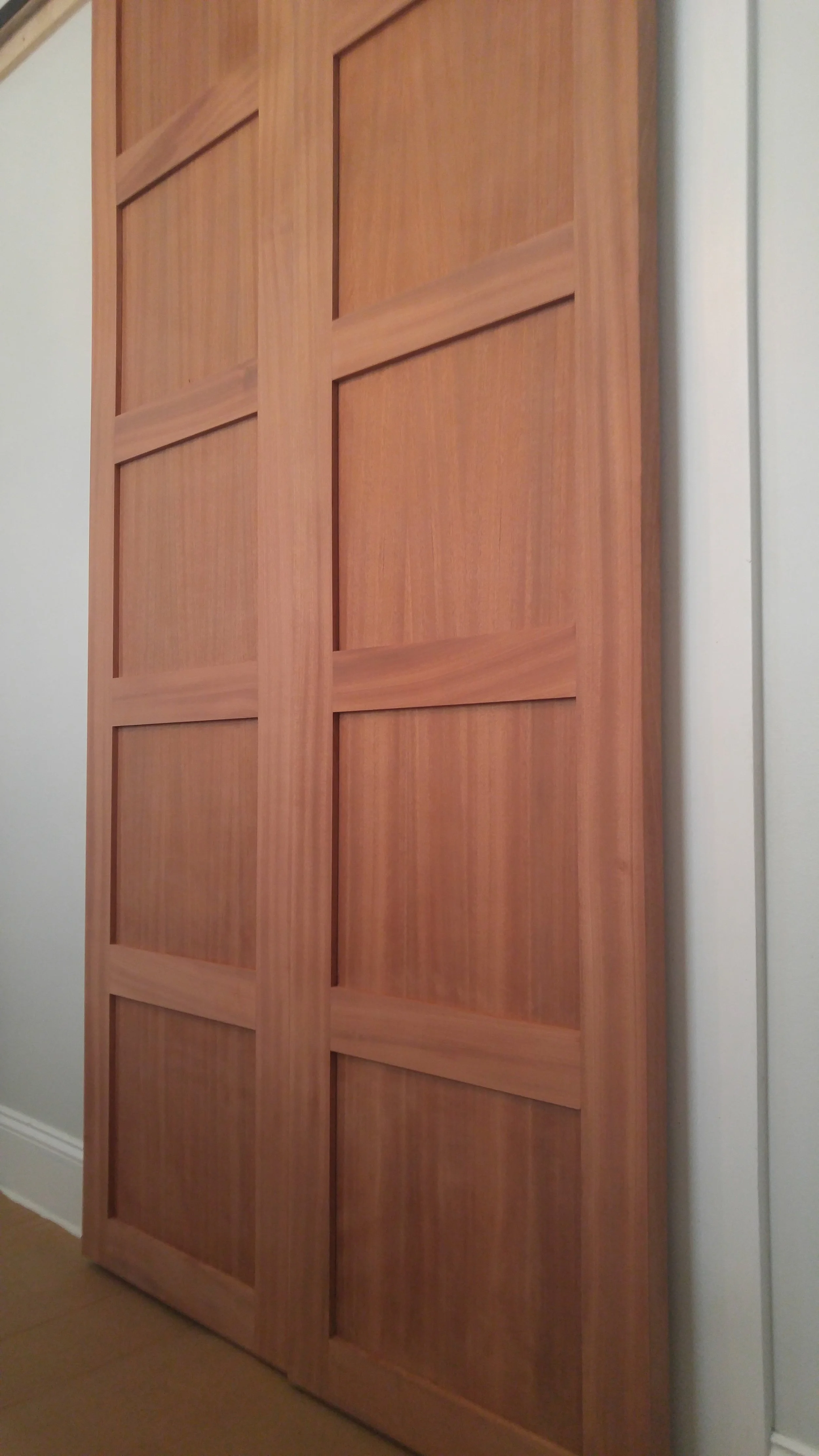 Custom sapele sliding door with a grid pattern, installed against a white wall, on a hardwood floor.