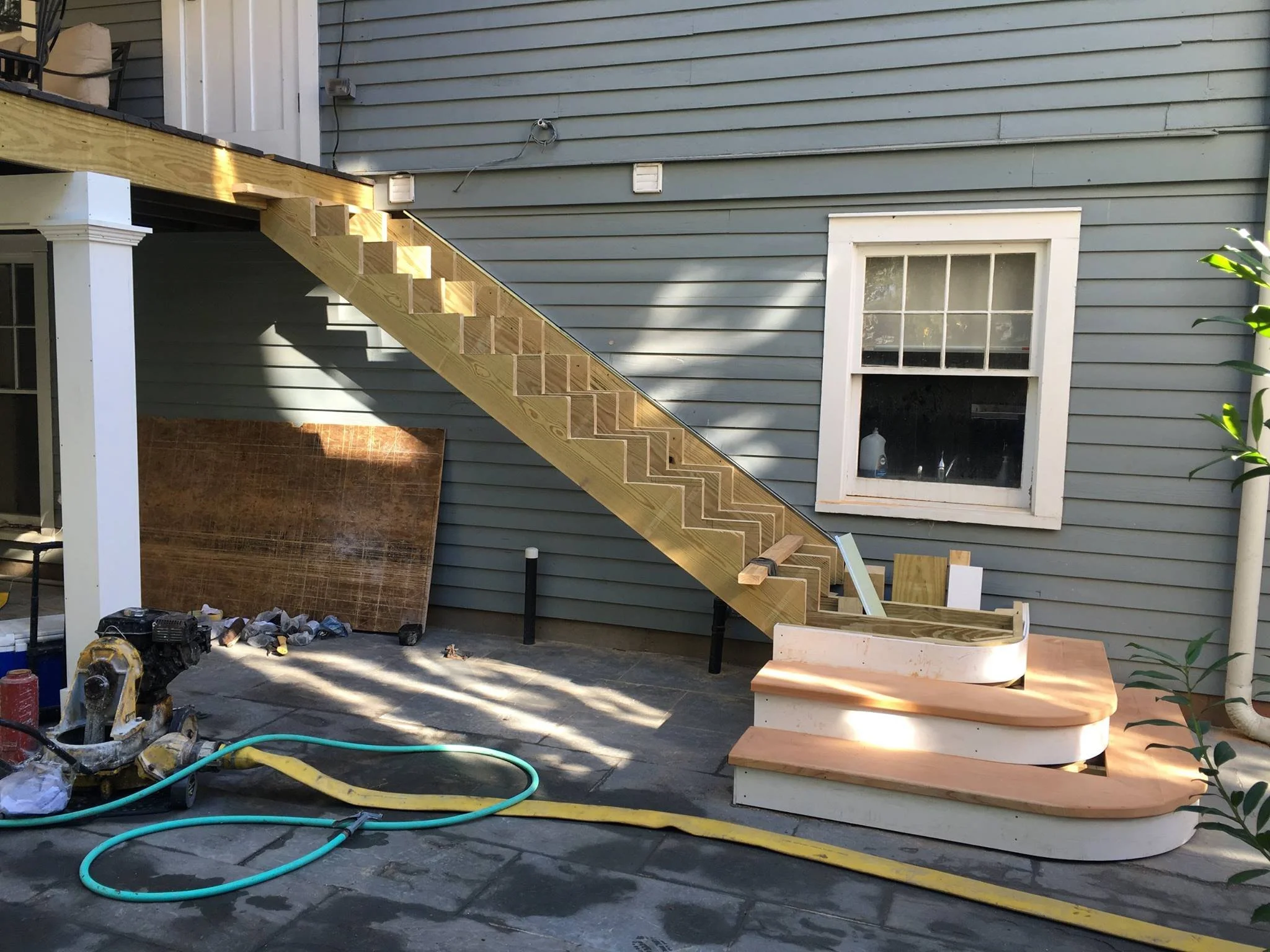 custom built wooden staircase under construction outside a house, with curved steps.