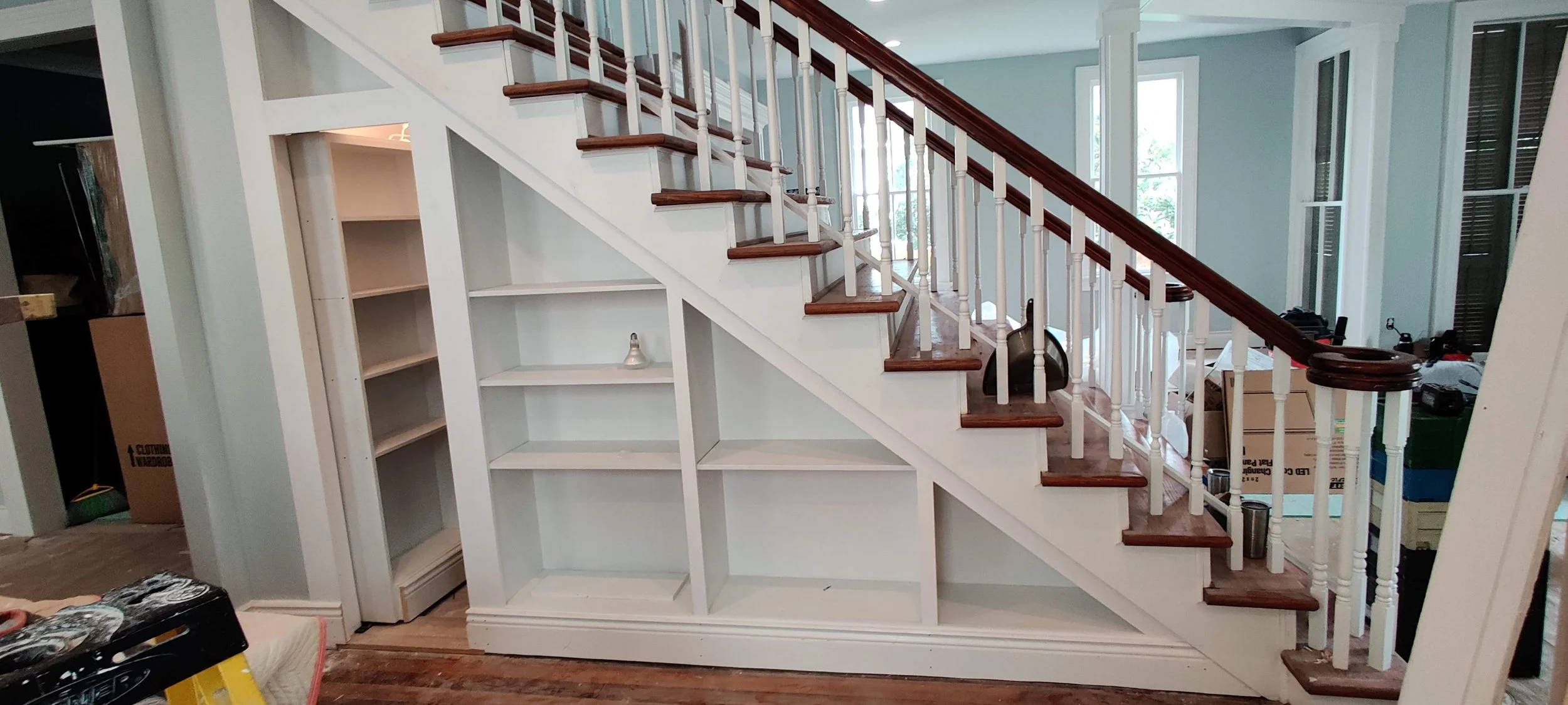 Interior of a house showing a staircase with a white base, dark wood steps, and a white and dark wood railing. There are open shelves built into the staircase base.
