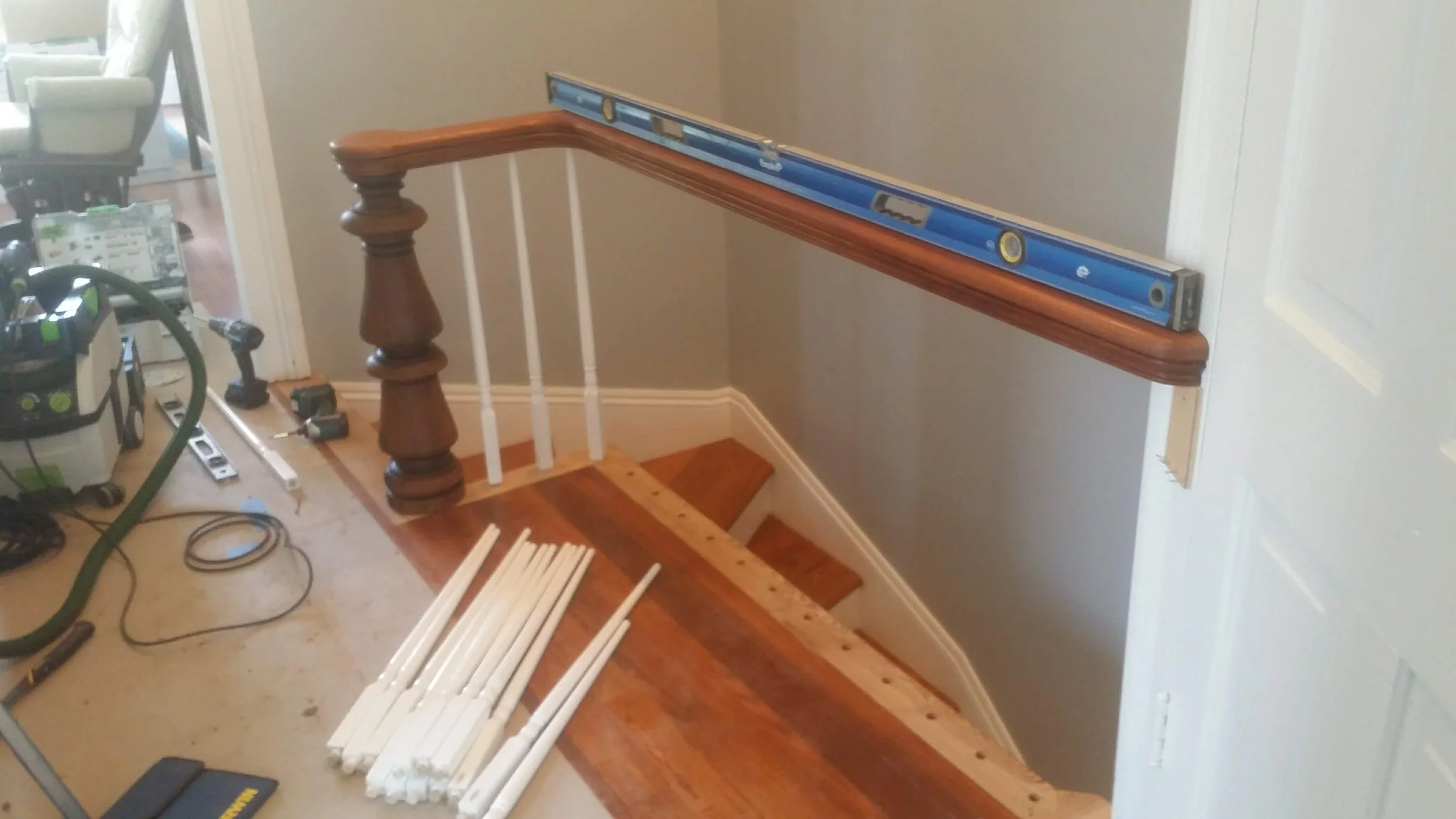 Indoor staircase with wooden handrail and white balusters under construction, with tools and white spindles placed on the floor.