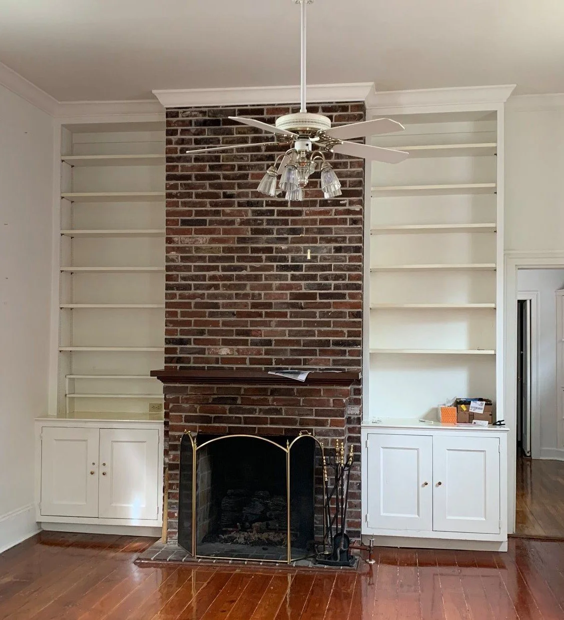Living room with a brick fireplace, white built-in bookshelves on both sides, and a ceiling fan with light fixtures.