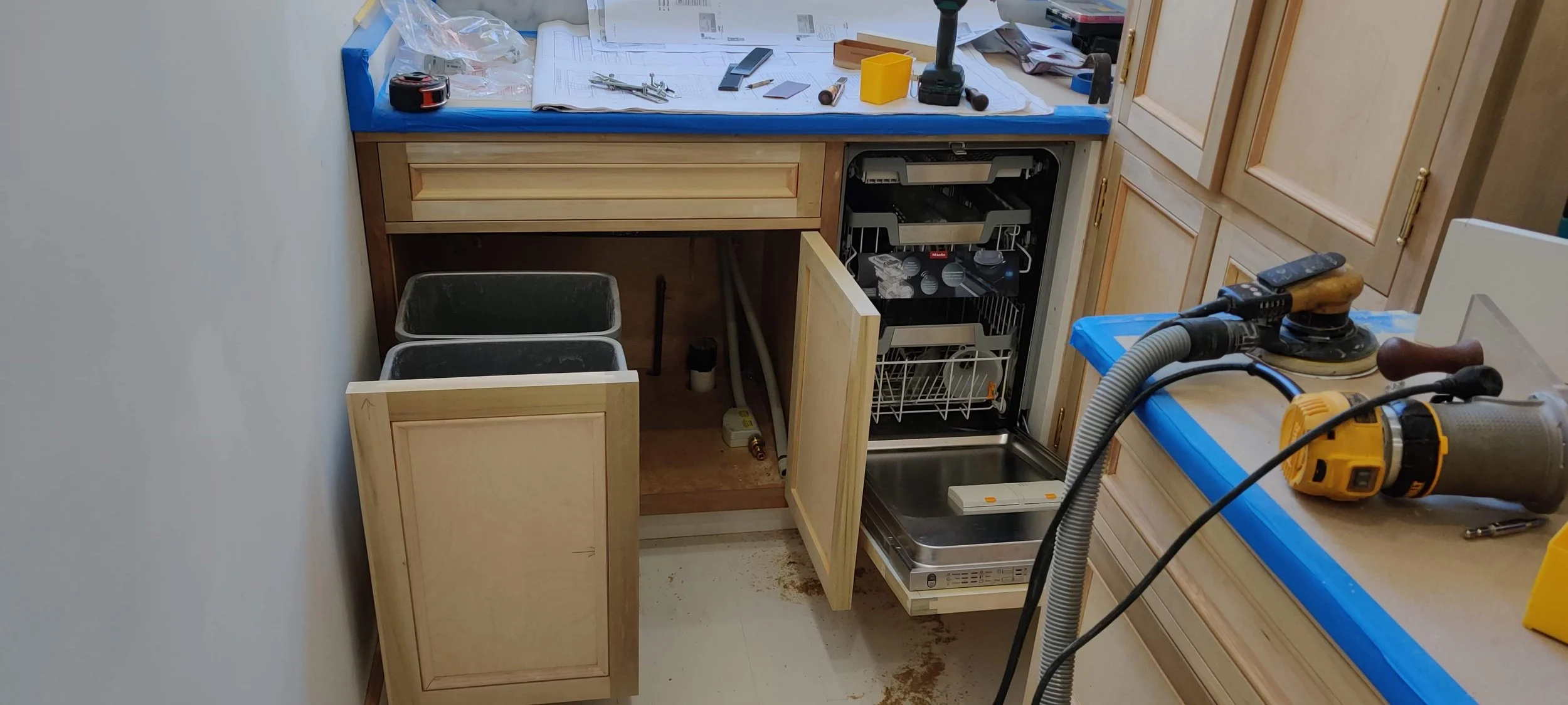 Kitchen cabinetry under renovation with open cabinets, tools, and a dishwasher.