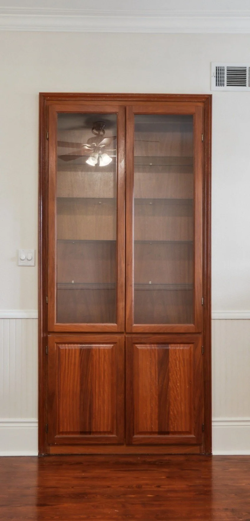 Custom built-in china cabinet with glass doors and wooden doors below, in a room with hardwood floor and white walls.