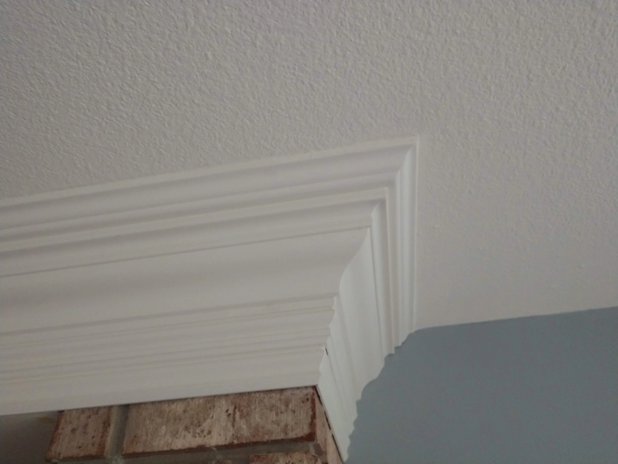 Close-up of a wall corner with architectural molding and white ceiling, with brick wall visible at the bottom.