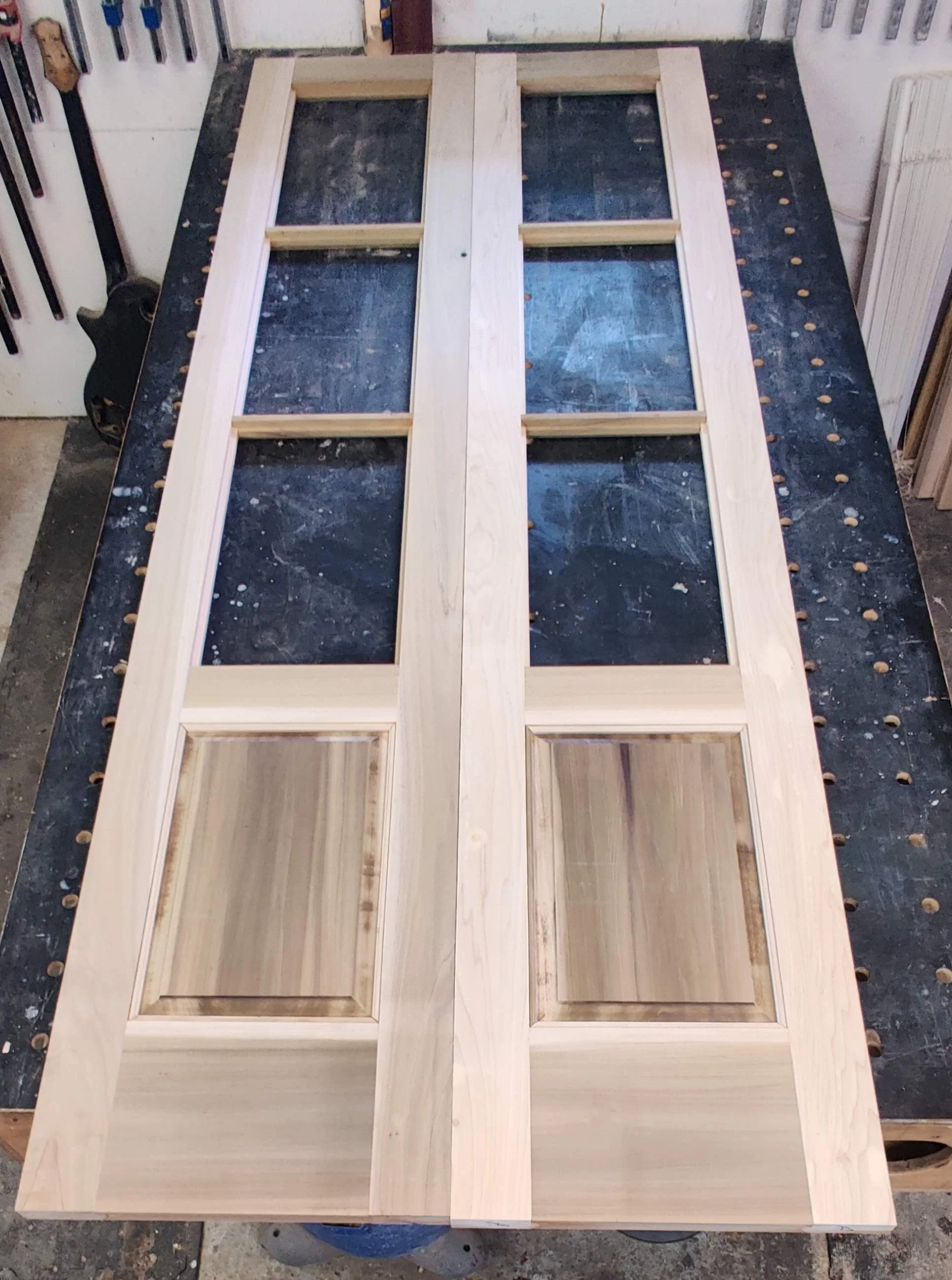 Wooden door with four glass panels and two raised panels at the bottom, lying flat on a workbench in a woodworking shop.