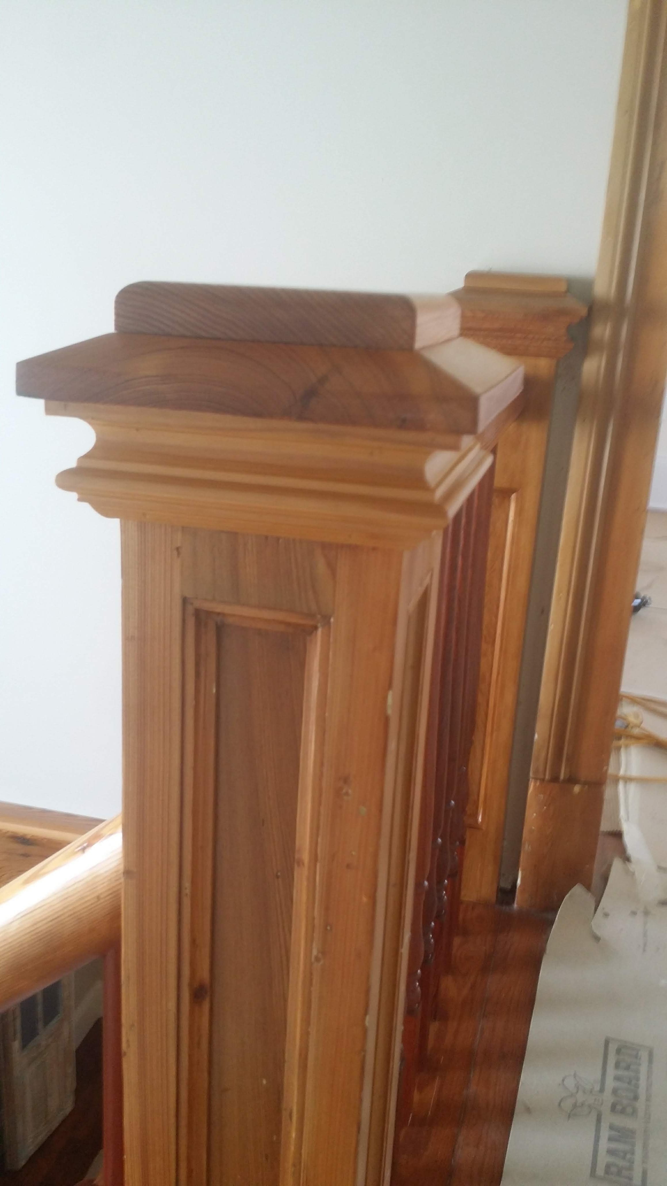 Close-up of a wooden staircase post or newel with detailed molding and finish, part of a stair railing in a home interior.