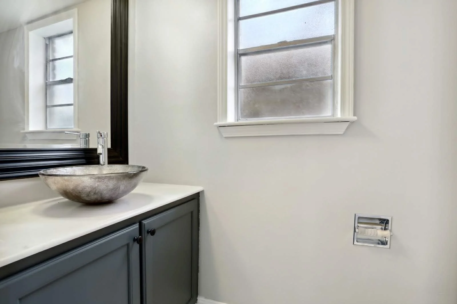 Bathroom with a gray vanity, a metallic vessel sink, a large mirror with a black frame, a window.