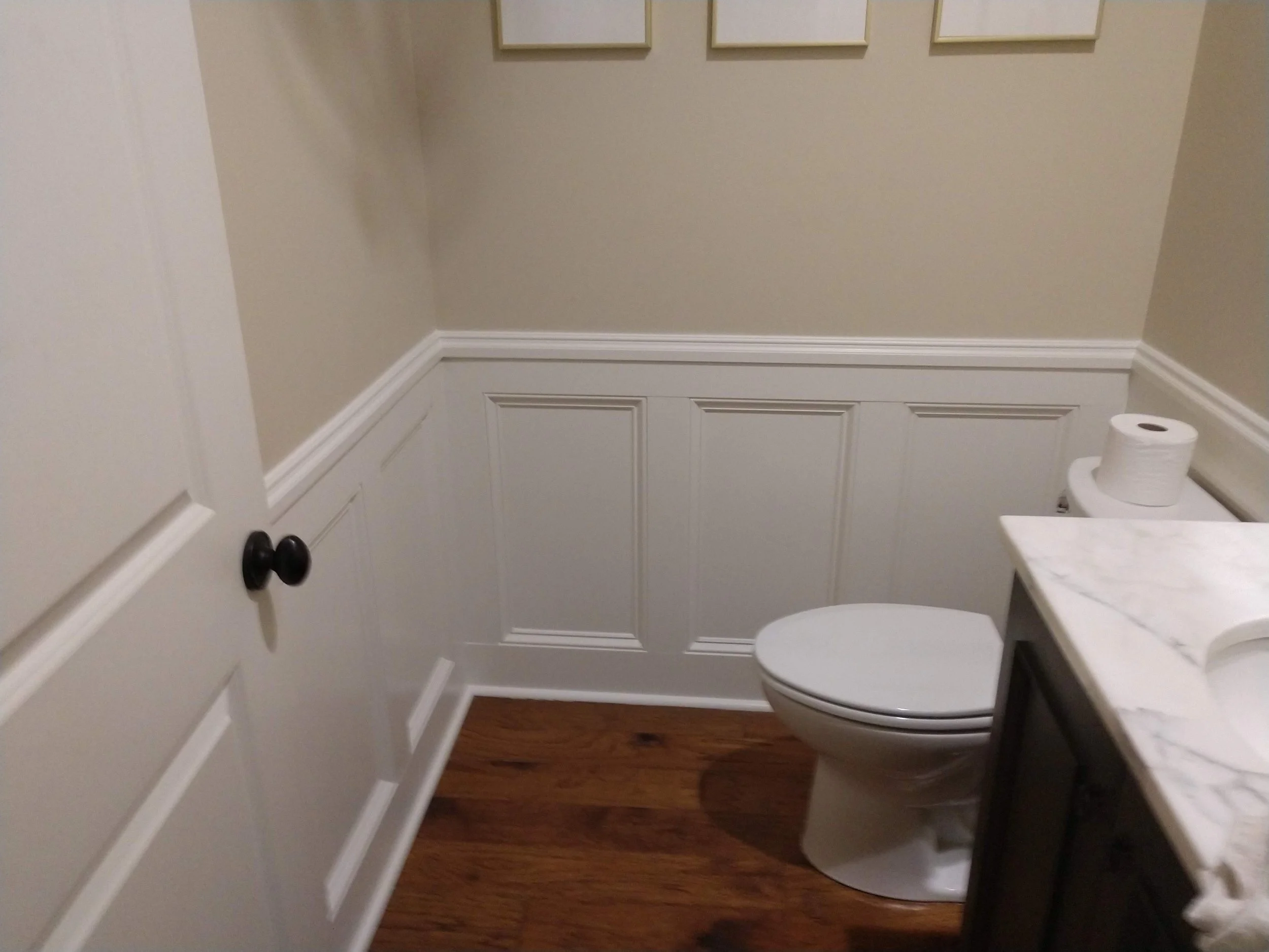 A small bathroom with beige walls, custom white wainscoting, 