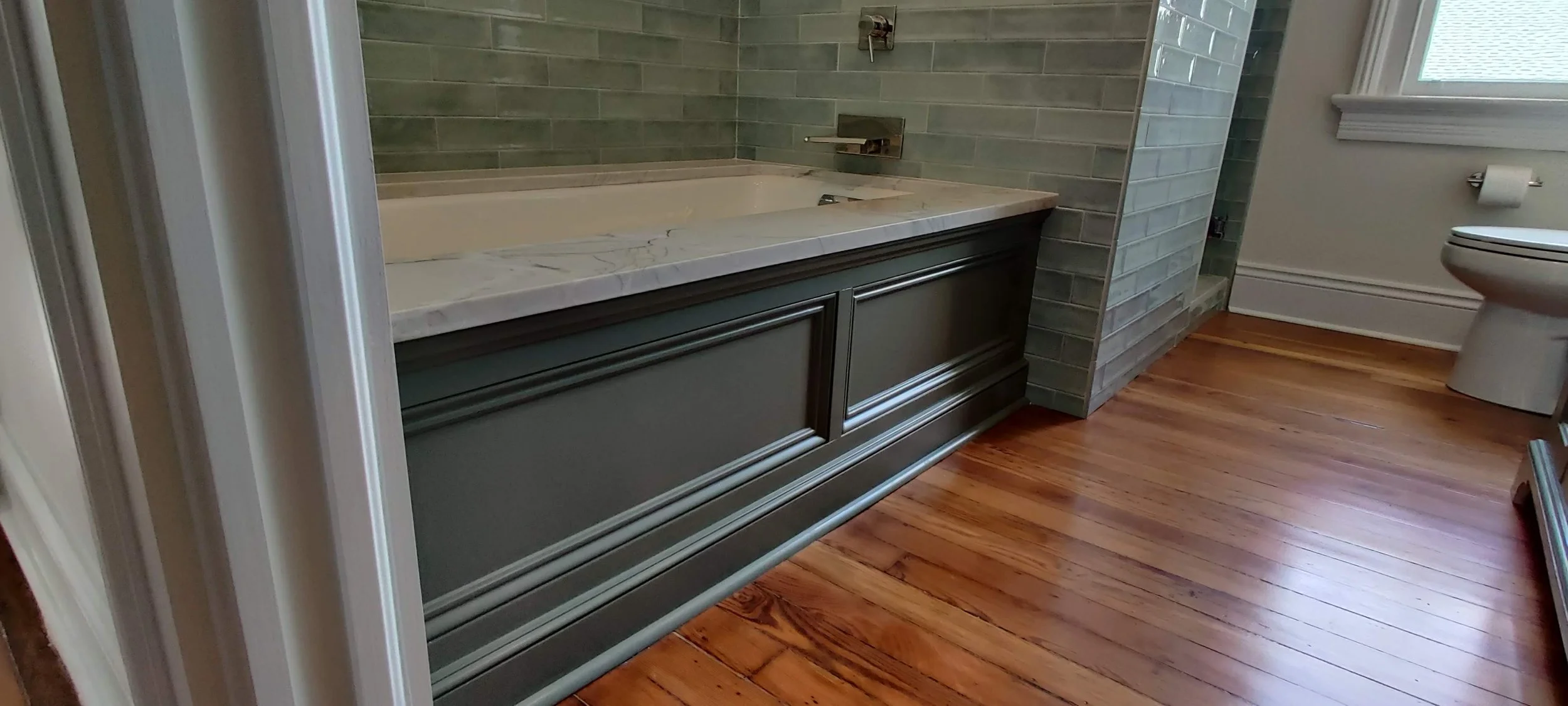 Bathroom with a marble-topped vanity, green tile walls, and hardwood floors,