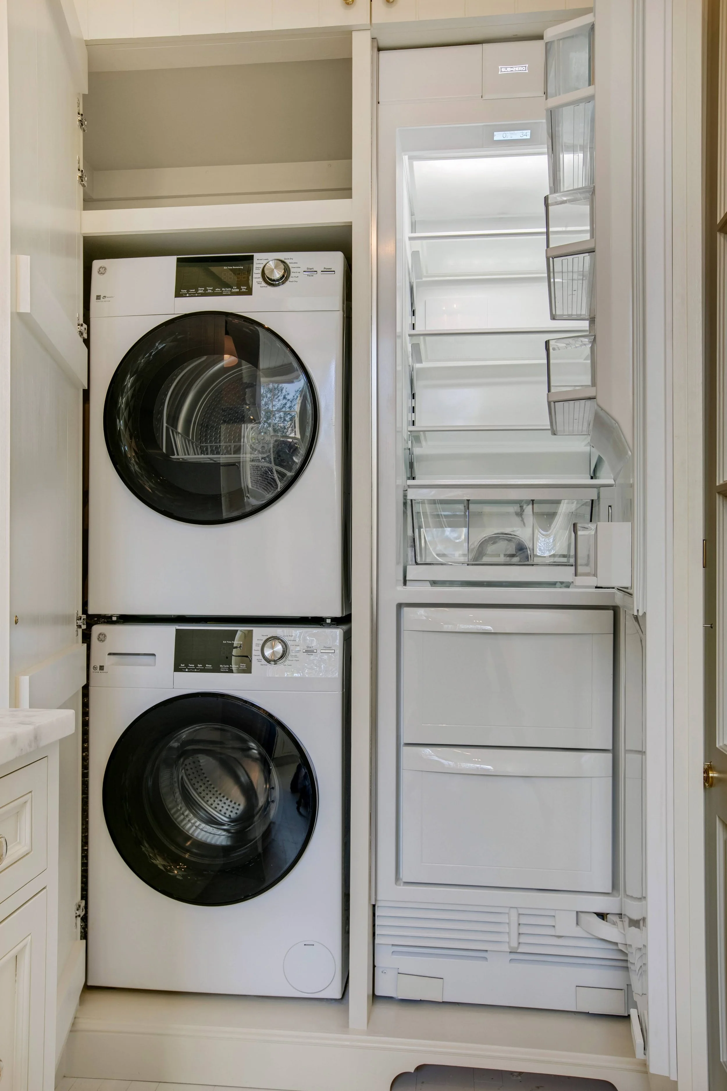 Custom built cabinet houses a stacked washer and dryer and a refrigerator