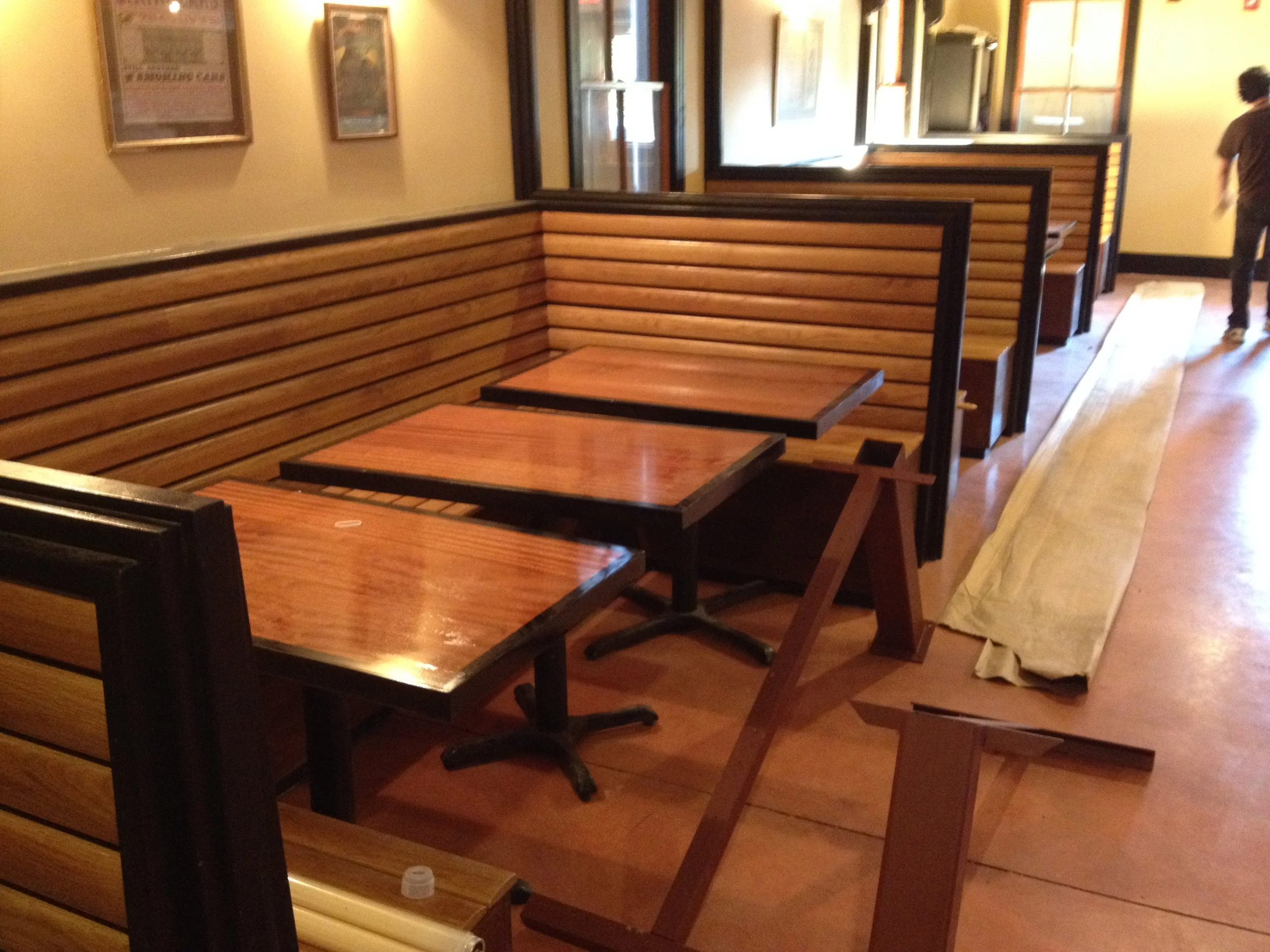Booth seating at a restaurant with wooden tables and partitions, and a person walking in the background.