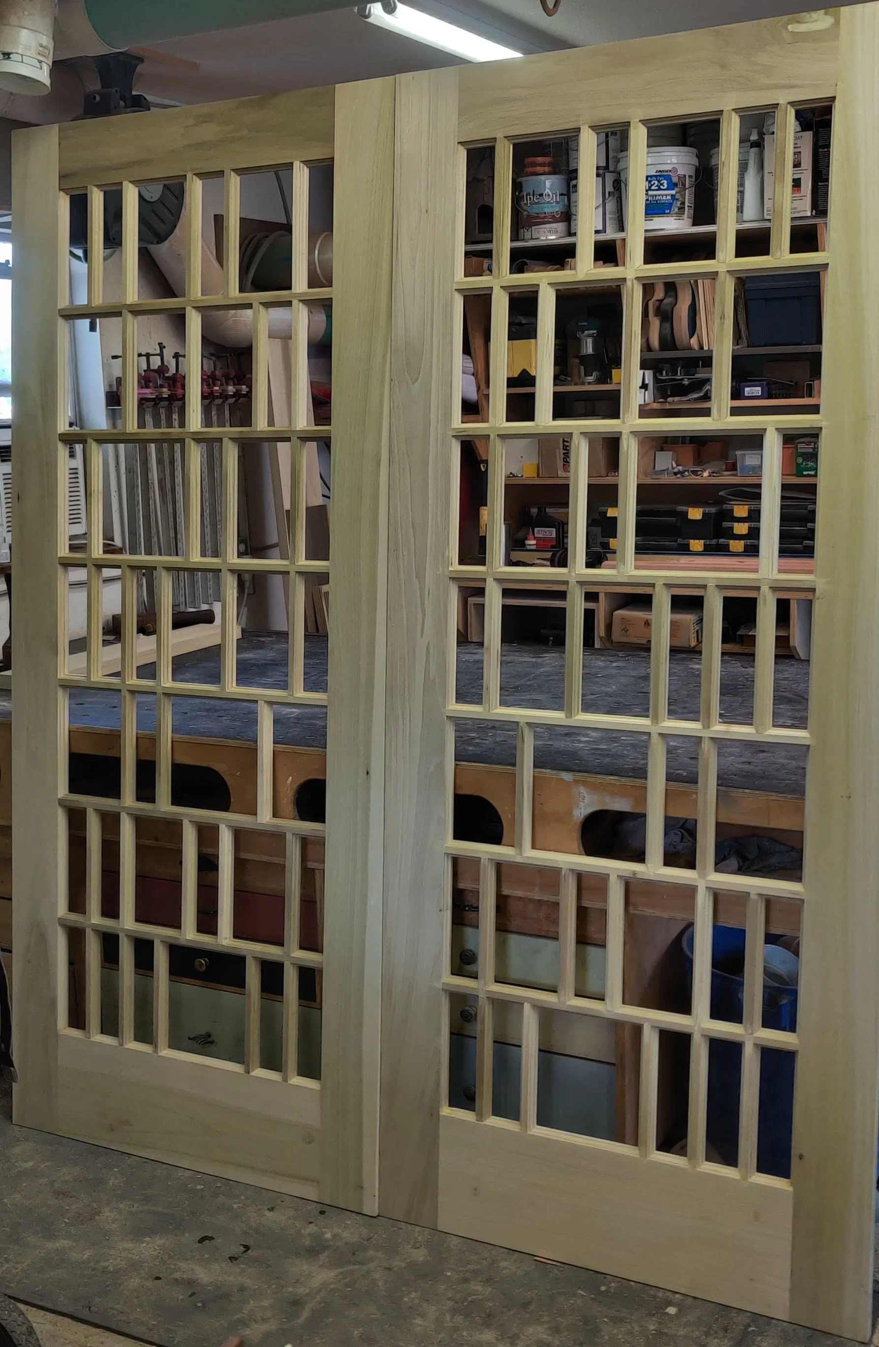 Unfinished wooden French doors with glass panels in a workshop.