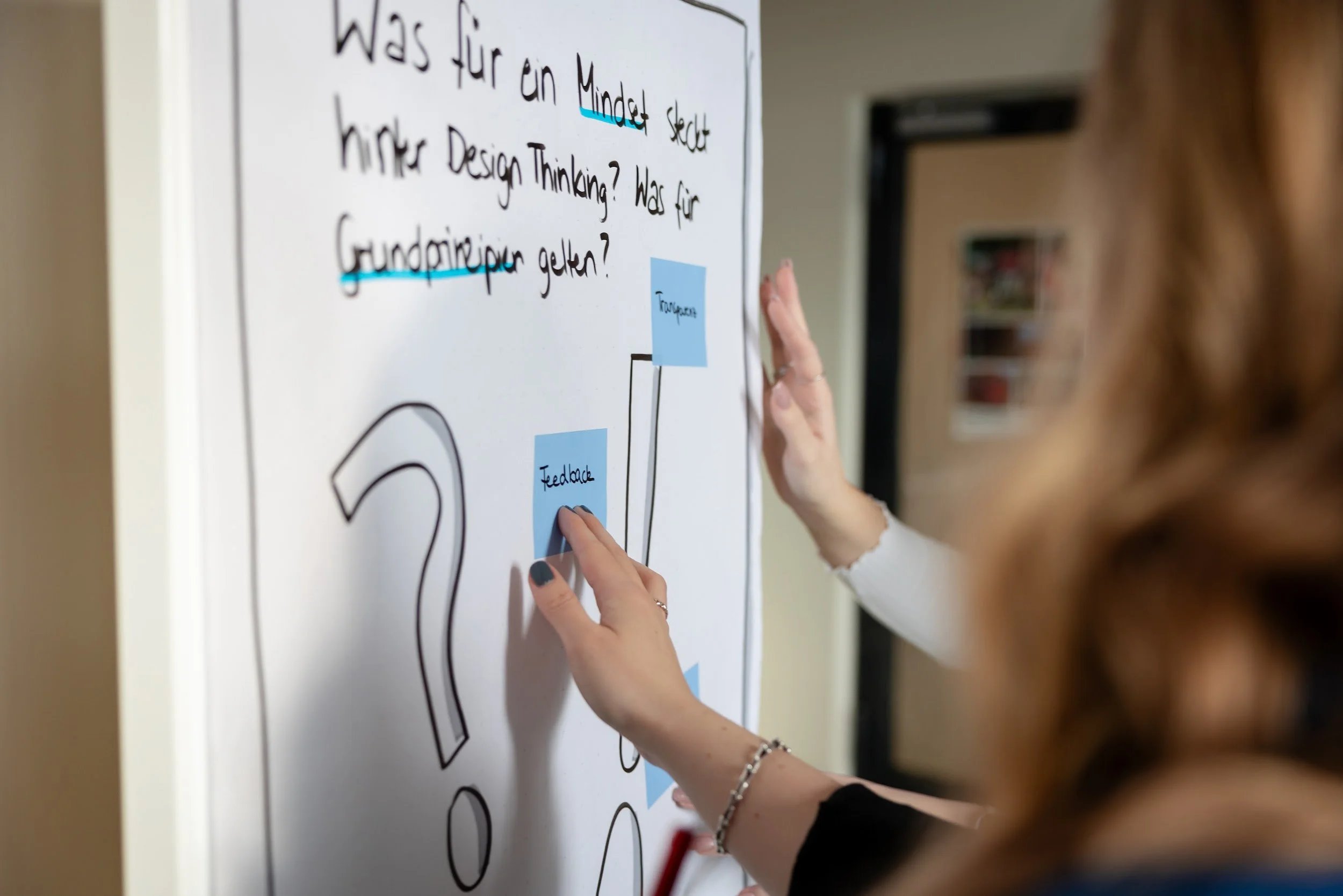 Person schreibt auf einen Whiteboard mit blauen Post-its, die eine Präsentation oder Diskussion unterstützen.