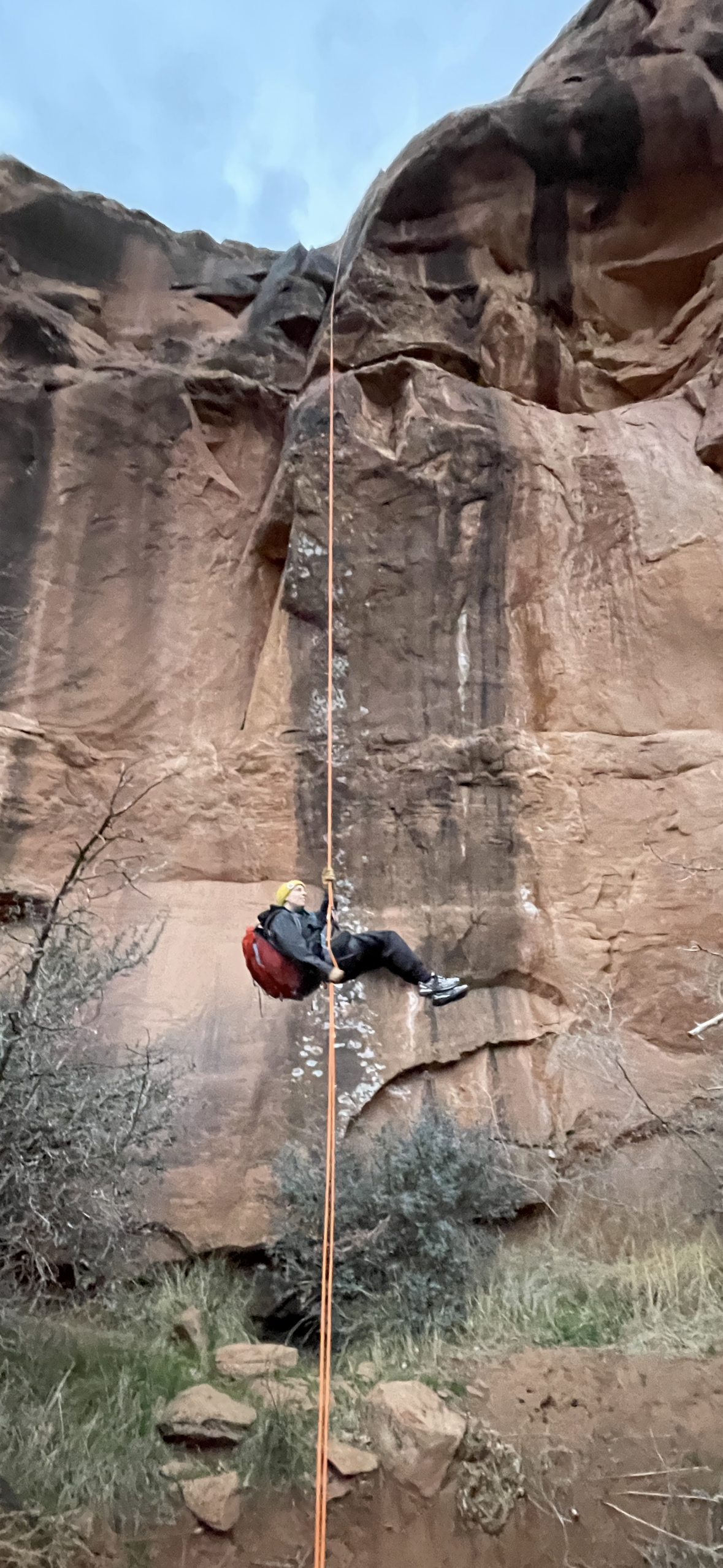 Rock climber rappelling down a tall cliff in a yellow helmet, illustrating prolonged outdoor exposure to sun, wind and dry air.