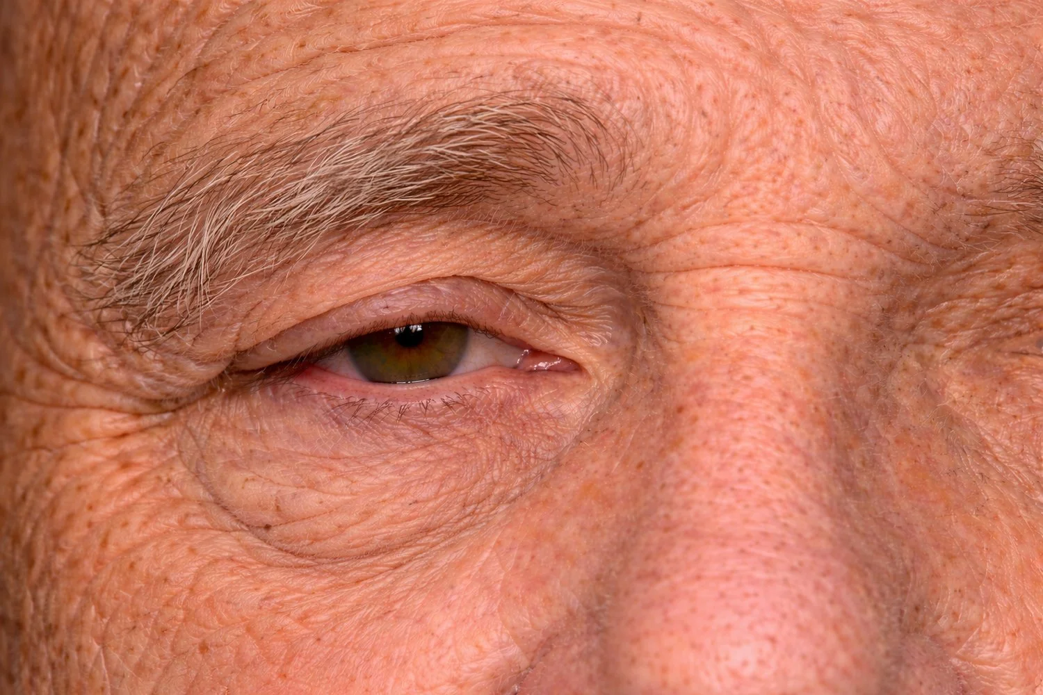 Close-up of an elderly person's face focusing on the eye with visible wrinkles and gray eyebrows.