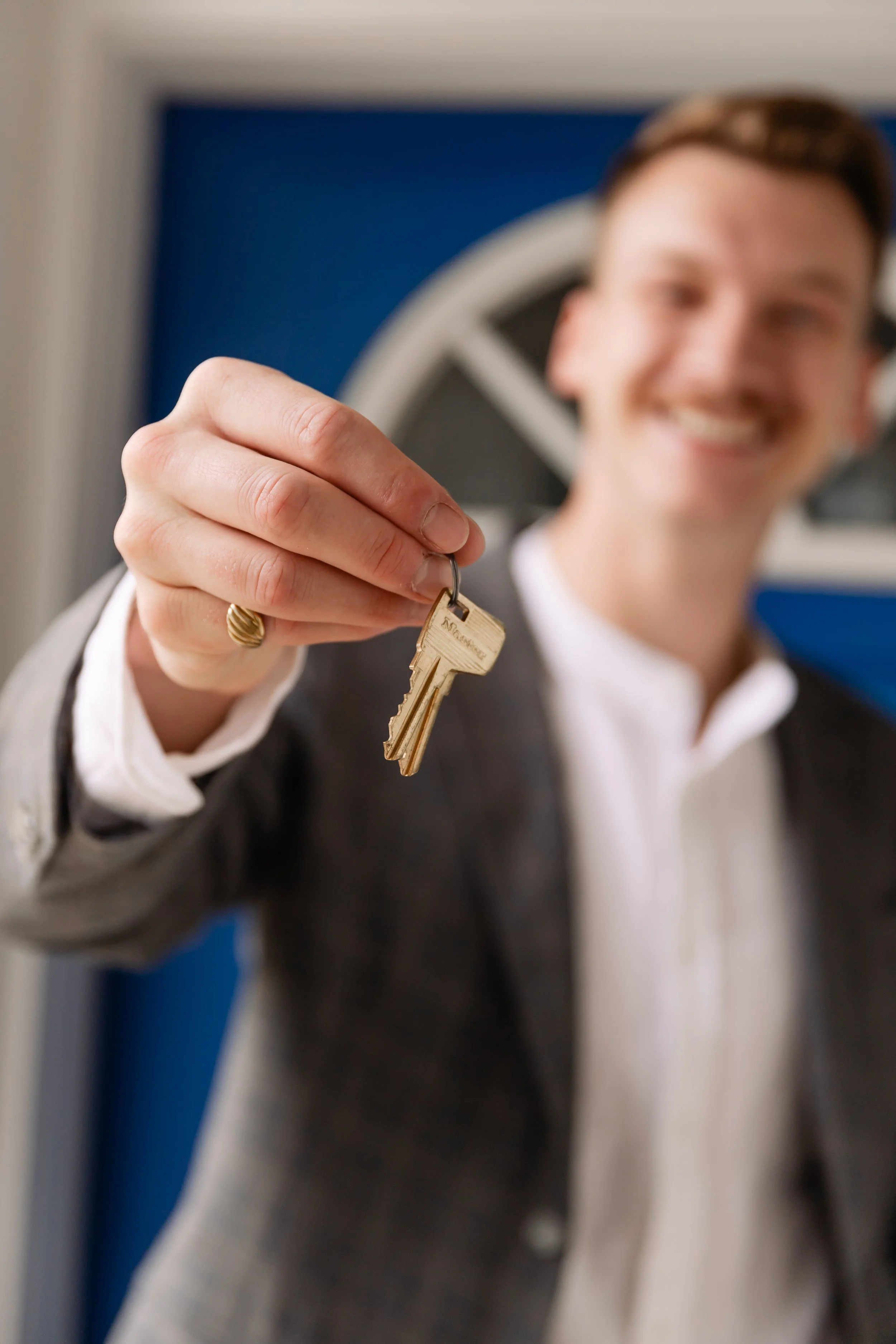 A smiling man in a suit holding a key in front of the camera.