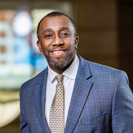 Portrait of a smiling man in a blue plaid suit and tie indoors.